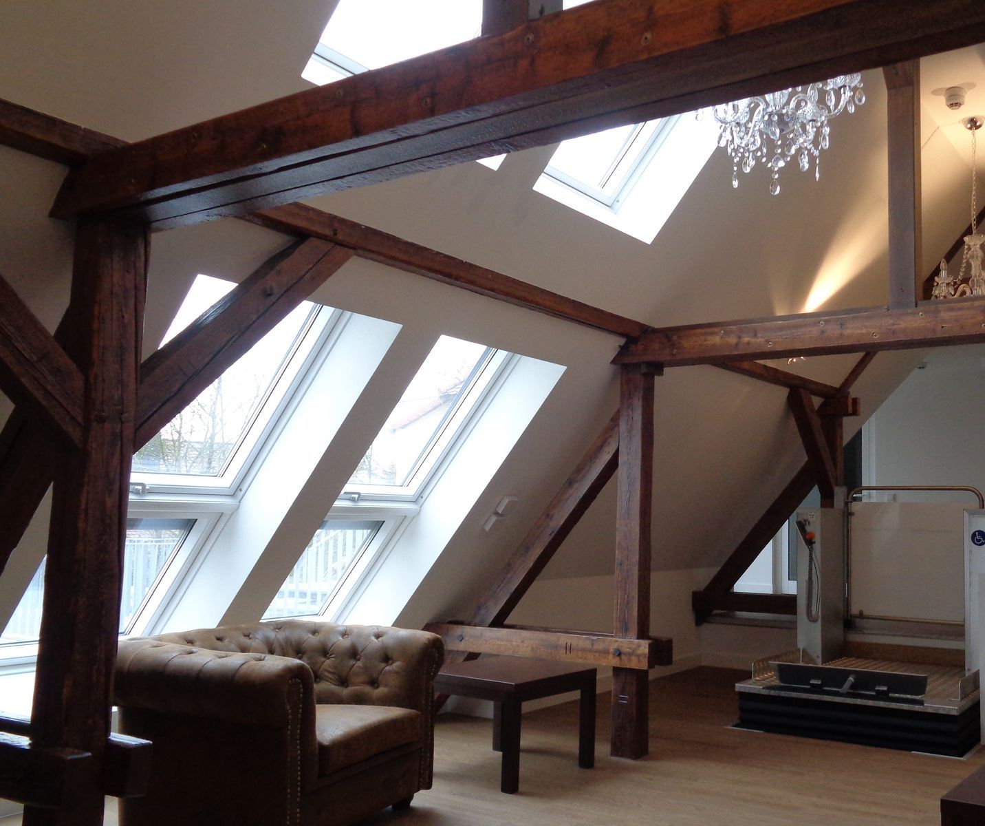 Loft-Interieur mit freiliegenden Holzbalken, Oberlichtern, Ledersessel und kleinem Couchtisch.