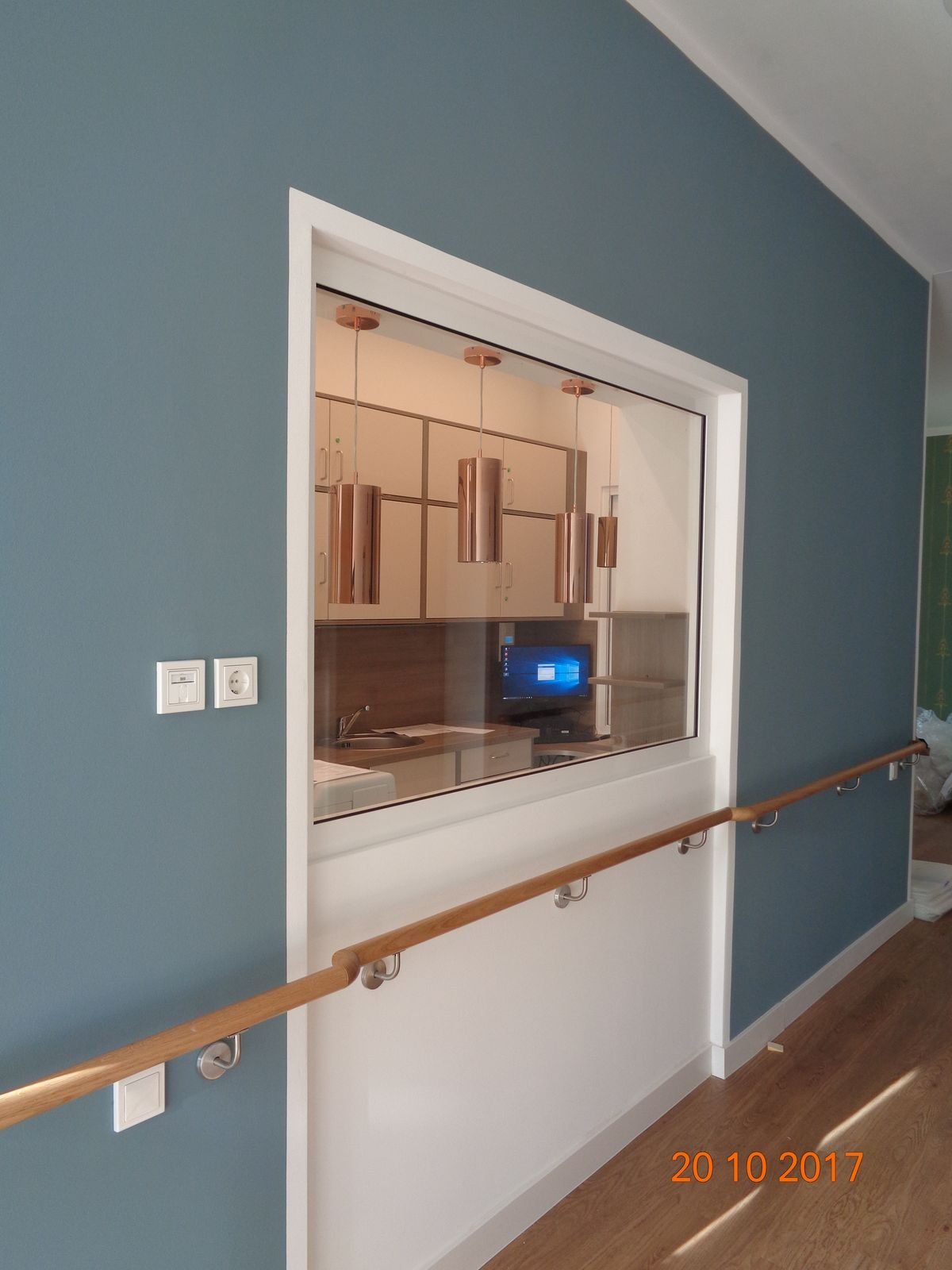 Fenster mit Theke und Handlauf; blaue Wand, weiße Zierleisten, durch das Glas sichtbare Kupferleuchten.