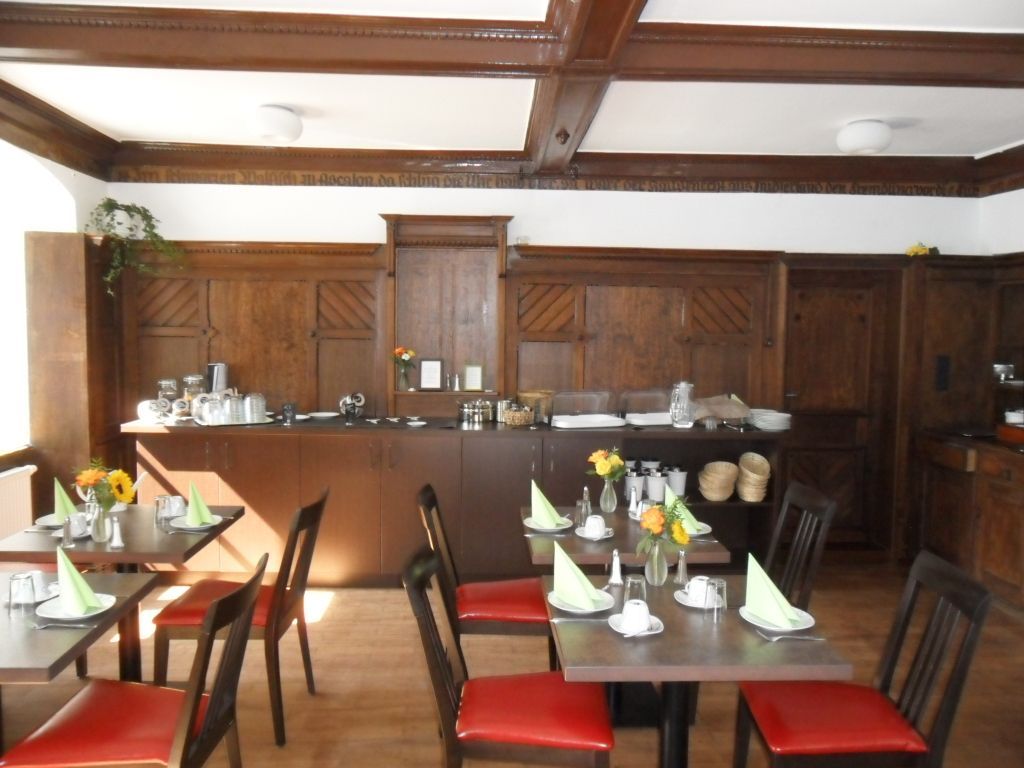 Frühstücksbuffet in einem holzgetäfelten Raum. Tische mit roten Stühlen sind für die Gäste gedeckt.