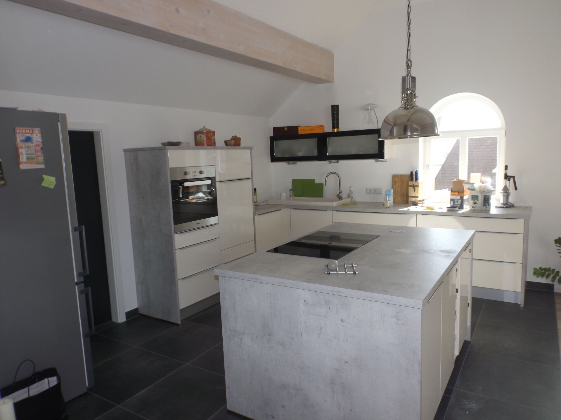 Moderne Küche mit Kochinsel, weißen Schränken, dunkelgrauem Boden und großem Fenster.