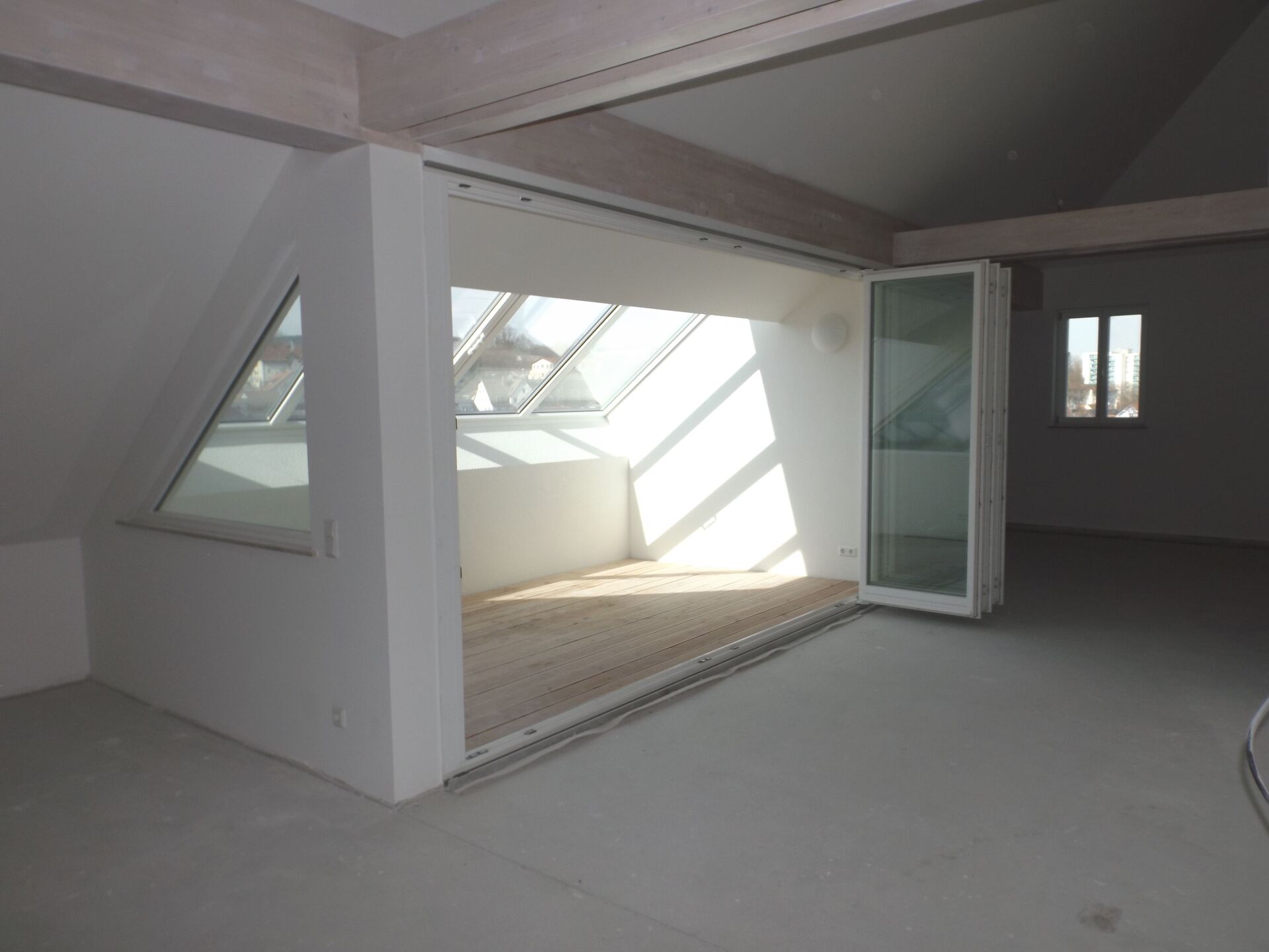 Helles Dachzimmer mit eckigem Oberlicht und Falttüren aus Glas, weißen Wänden und hellem Boden.