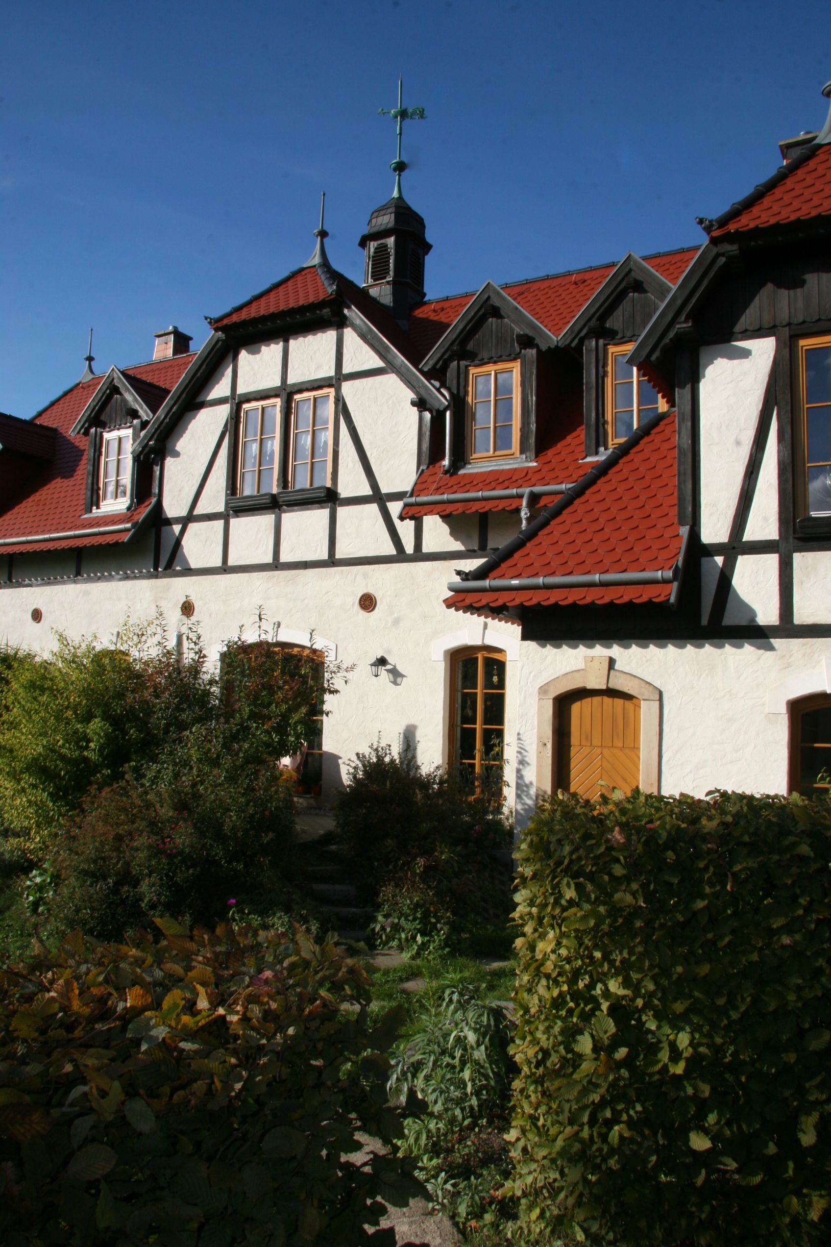 Ein Gebäude im Tudorstil mit weißen Stuckwänden, schwarzen Balken und rotem Ziegeldach unter blauem Himmel.