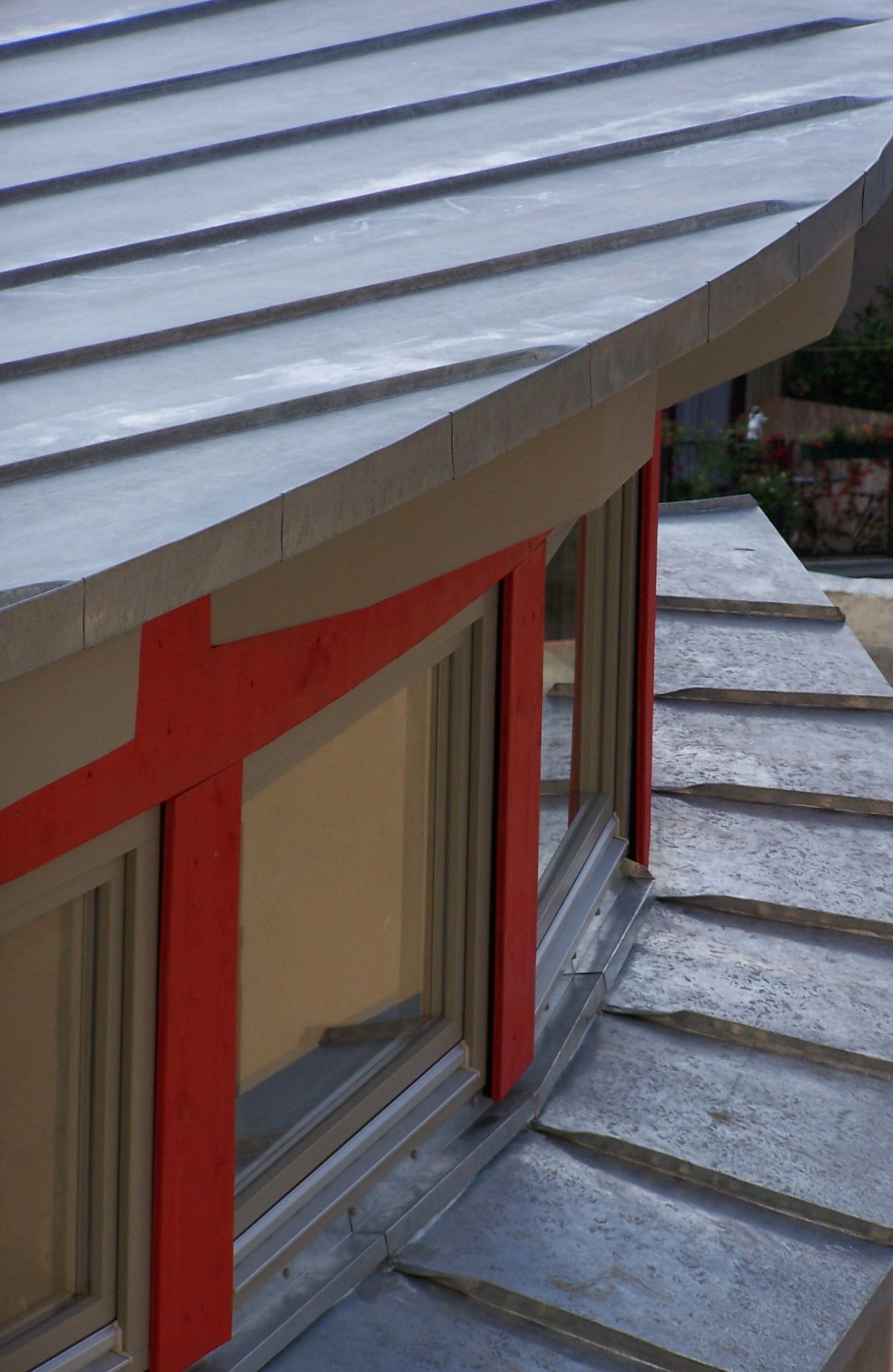 Graues Metalldach mit roten Akzenten über den Fenstern.