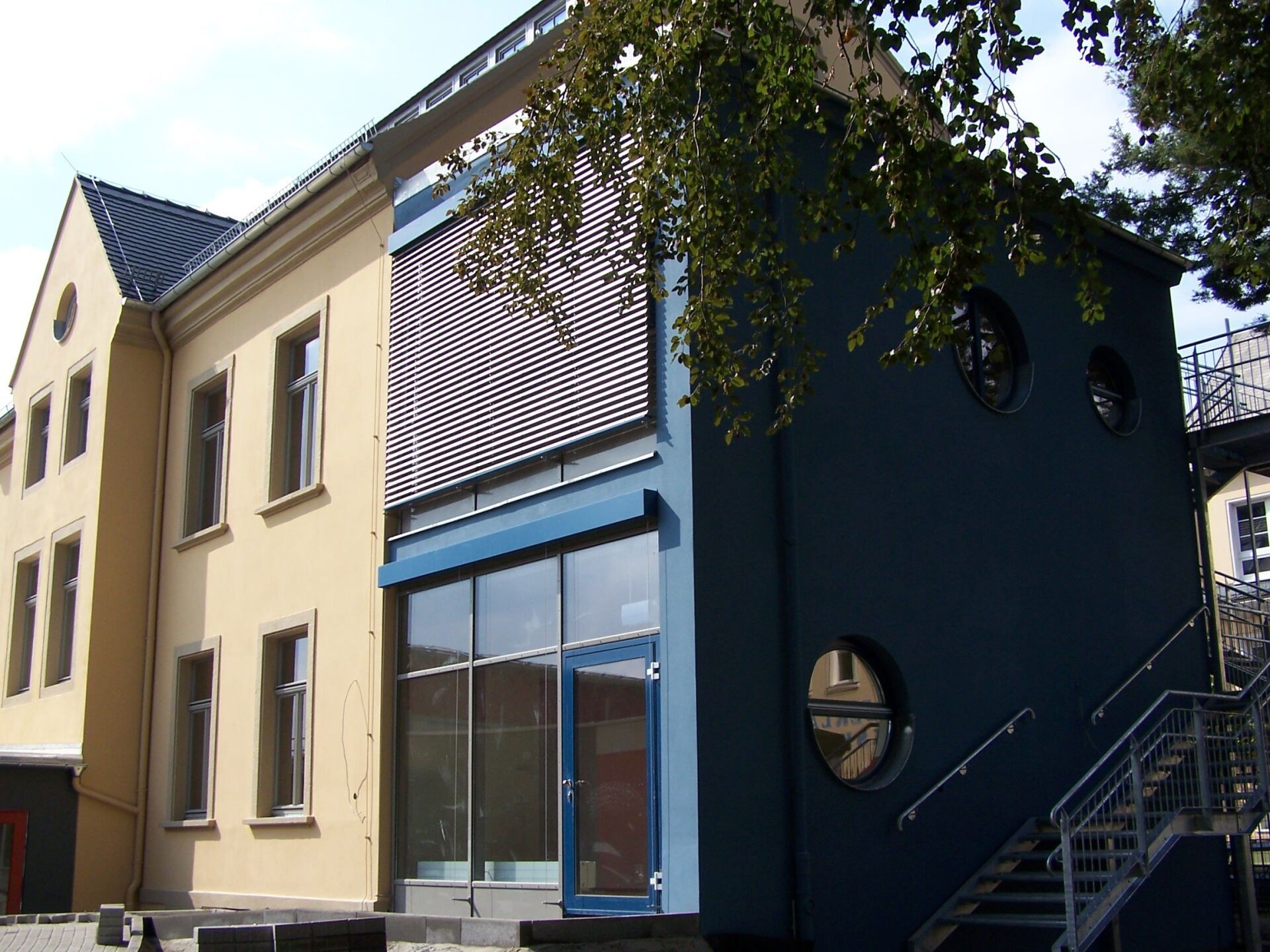 Gebäudefassade mit unterschiedlichen Farben und Architekturstilen: Gelb, Blau und Grau.