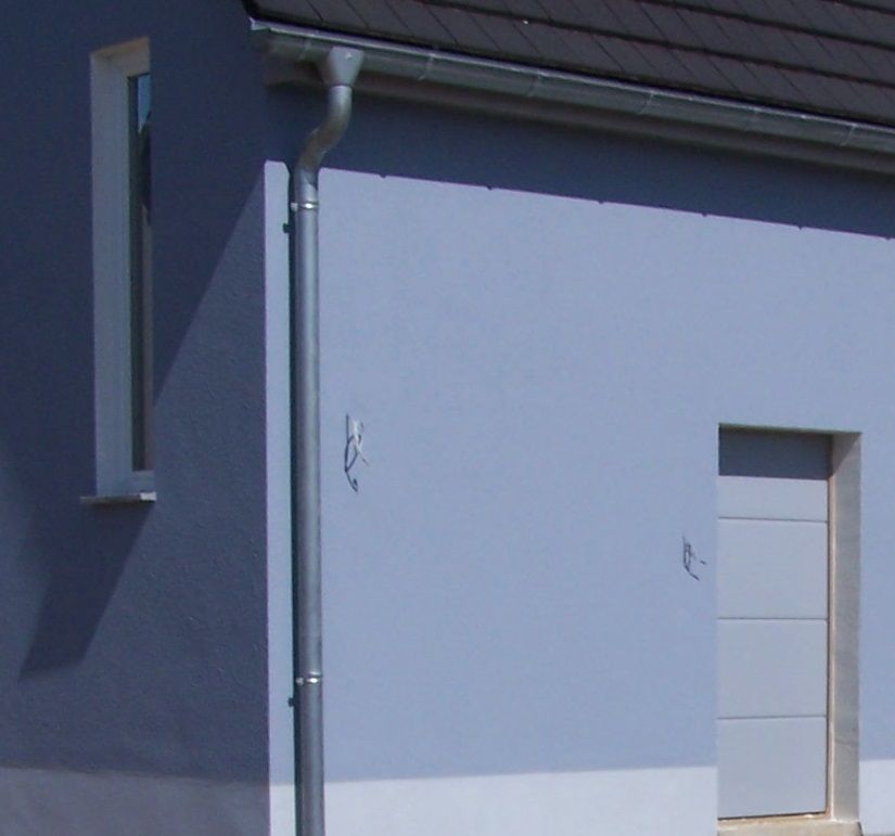 Blaue Gebäudefassade mit Fenster, Tür und Dachrinne.