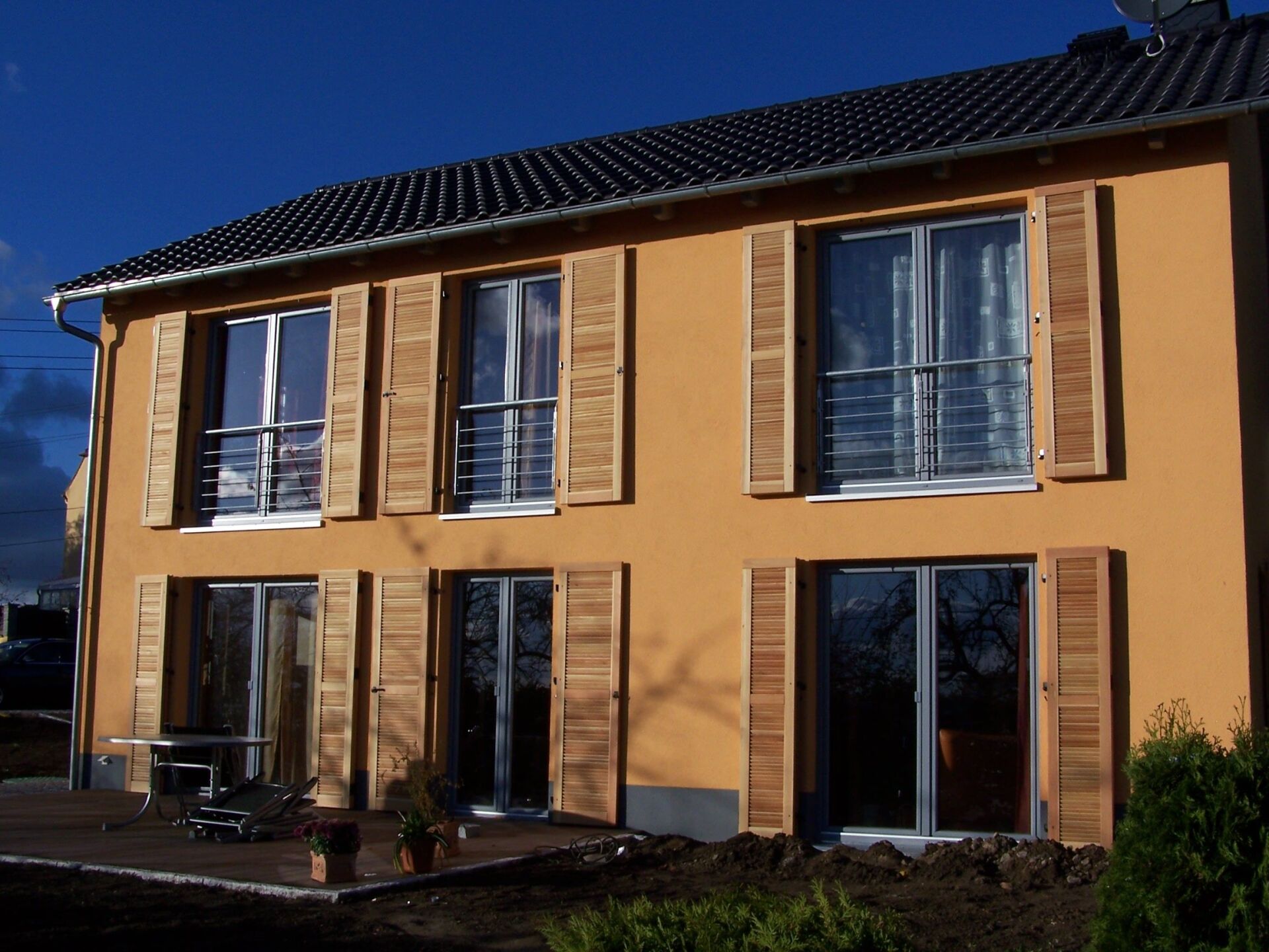 Zweistöckiges orangefarbenes Haus mit Holzfensterläden, strahlend blauer Himmel.