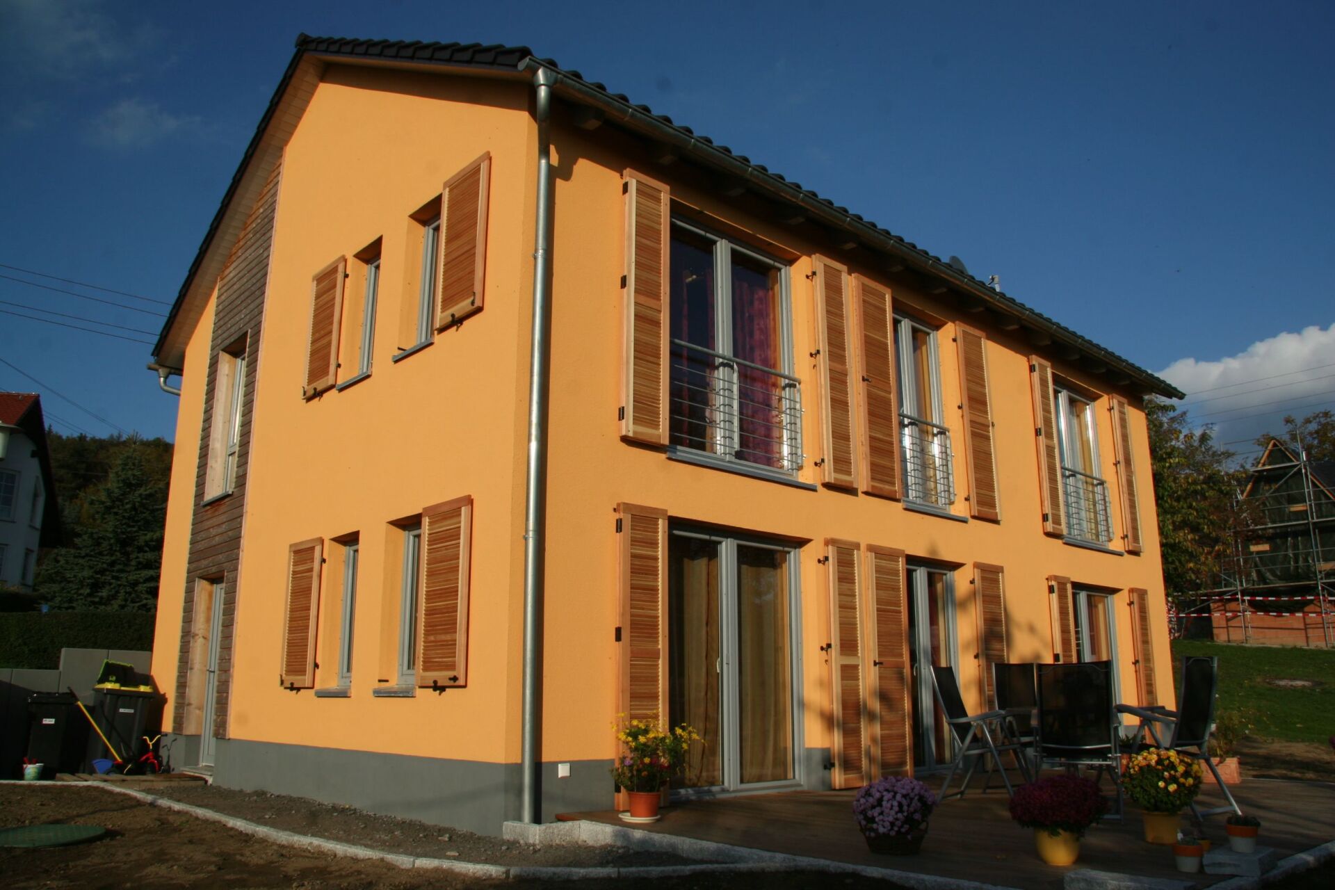 Zweistöckiges Haus mit orangefarbener Fassade, braunen Fensterläden und dunklem Dach an einem sonnigen Tag.