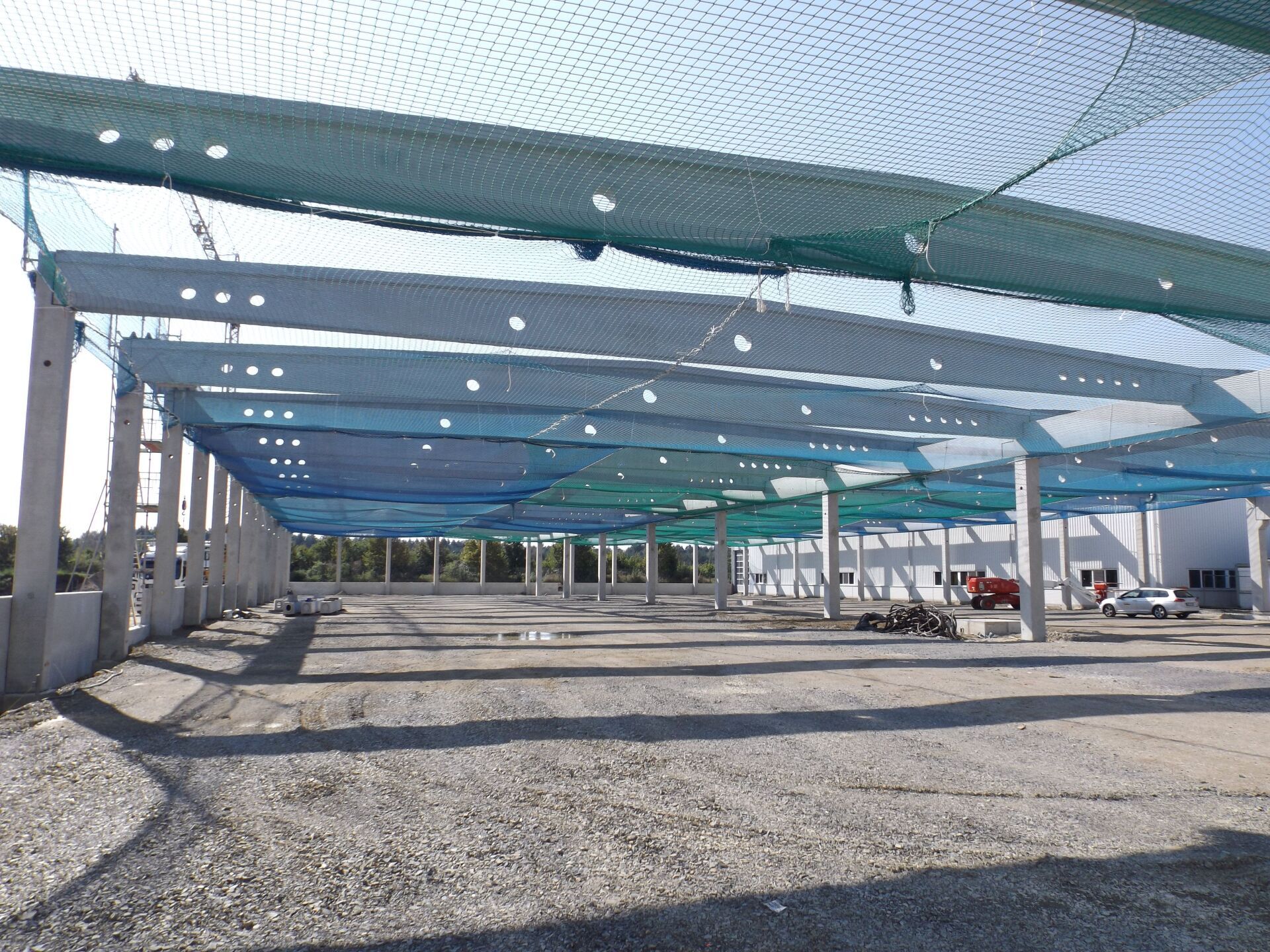 Innenansicht einer Baustelle mit Betonpfeilern, -trägern und Sicherheitsnetzen.