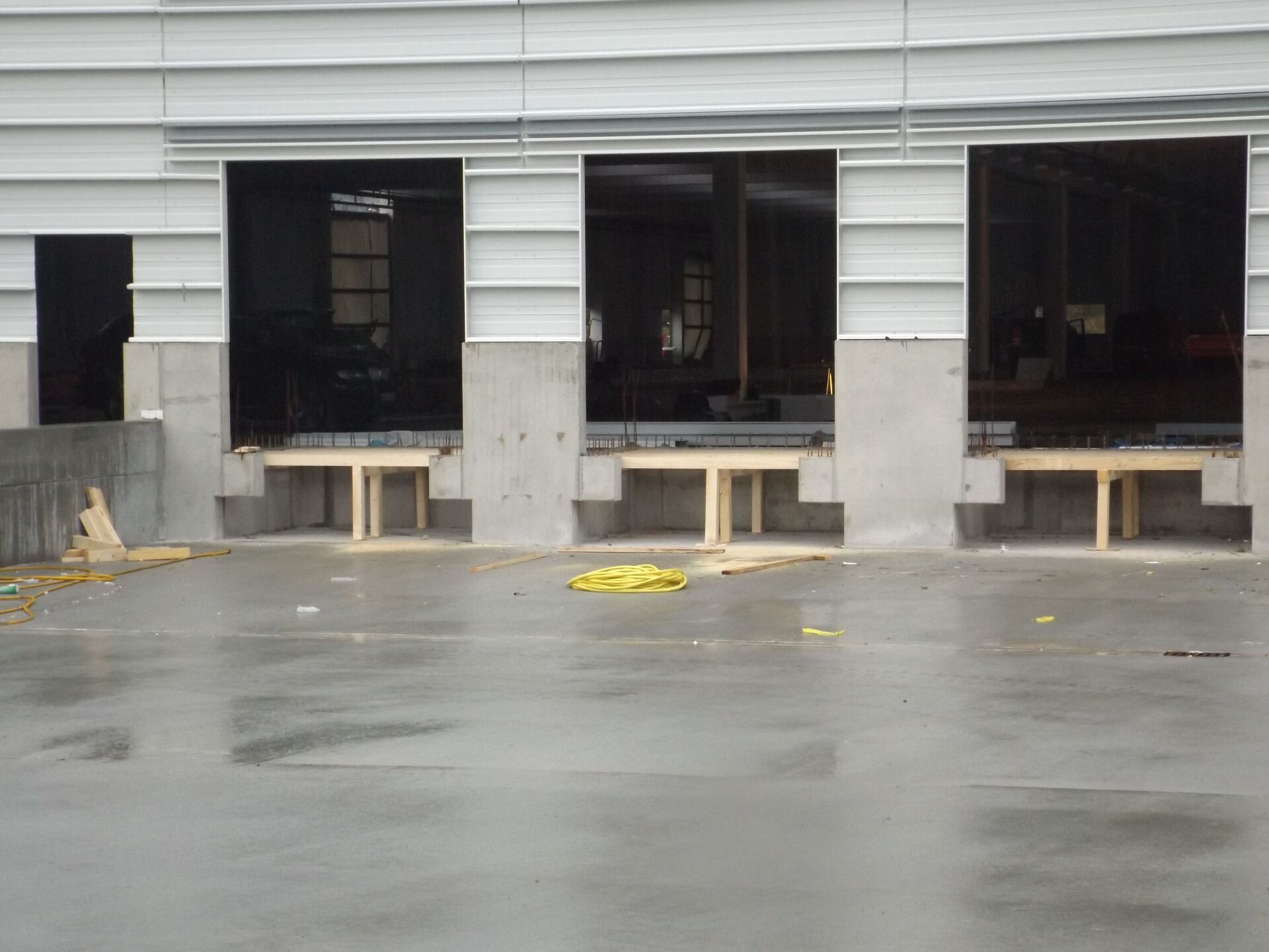 Laderampen in einem im Bau befindlichen Gebäude mit offenen Ladebuchten und Betonvorfeldern. Die nasse Betonoberfläche spiegelt sich von oben.
