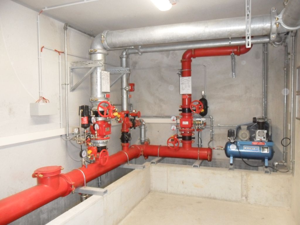 Rote Rohre und Komponenten einer Feuerlöschanlage in einem Technikraum mit einem Kompressor.