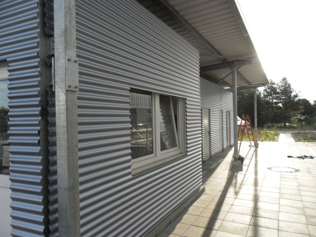 Gebäude aus Wellblech mit Fenster und überdachtem Gehweg.
