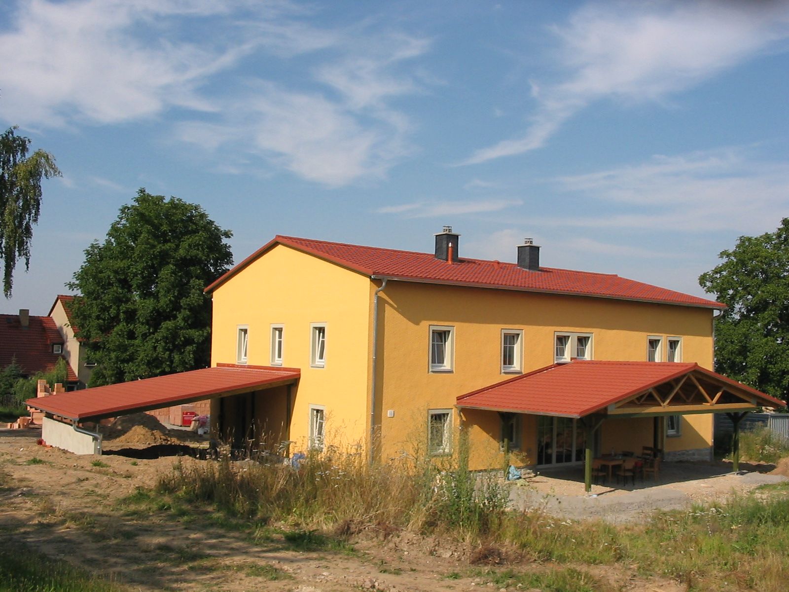 Gelbes zweistöckiges Gebäude mit rotem Dach und überdachtem Eingang; sonniger Tag.