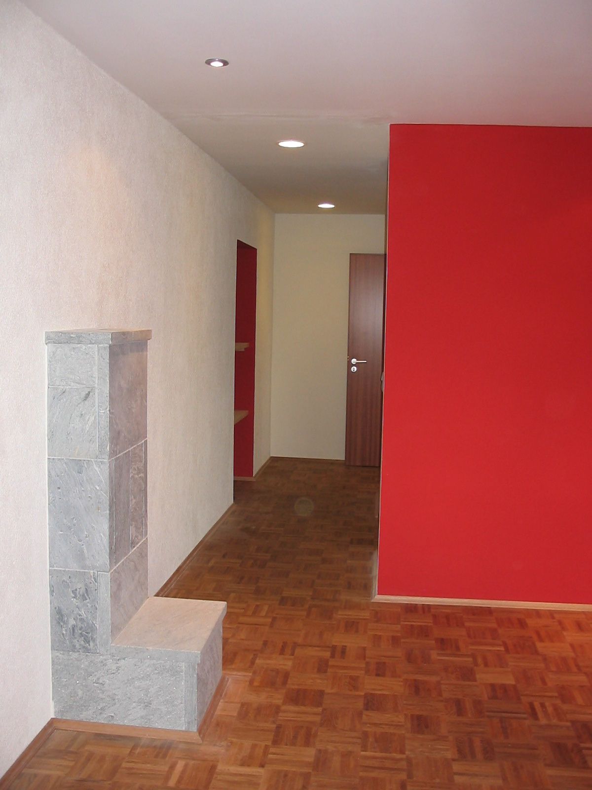 Innenansicht eines Zimmers mit roter Wand, grauem Kamin, Holzboden und Flur.