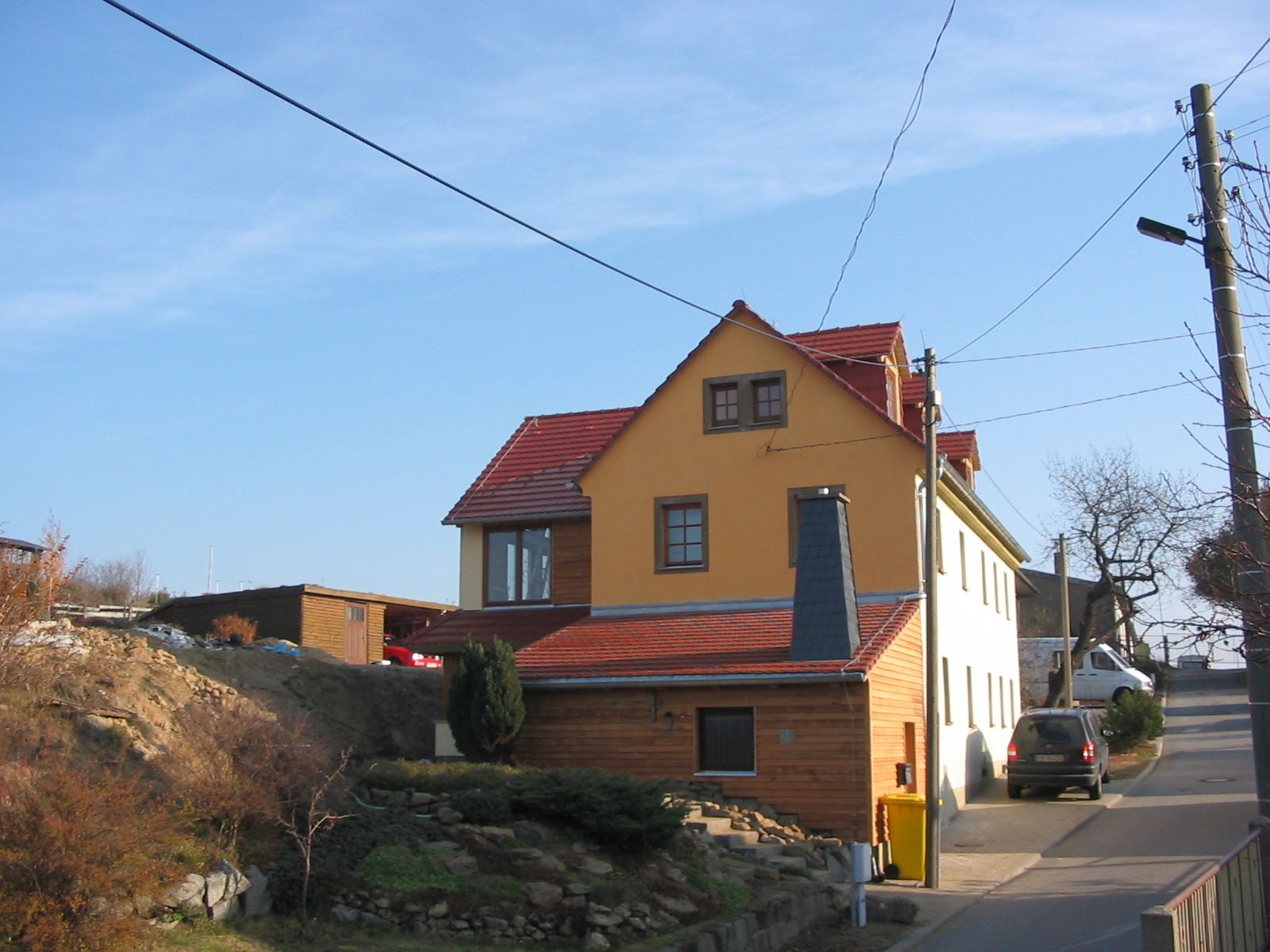 Ein Gebäude mit rot-gelbem Dach und braun-beigen Wänden in einer Straße mit blauem Himmel.