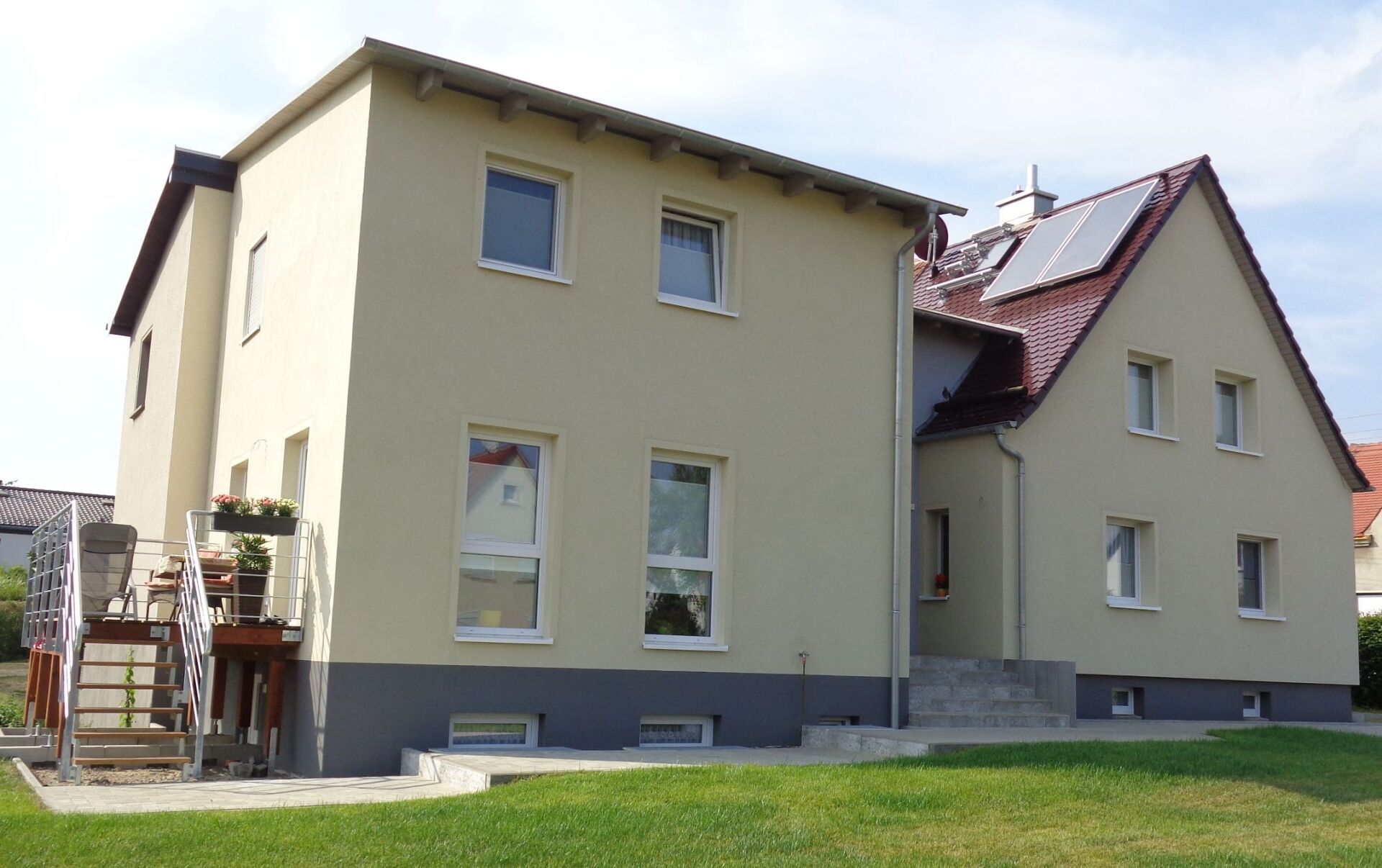 Beiges zweistöckiges Haus mit rotem Dach und Solarpaneelen, Fenstern und grünem Rasen.