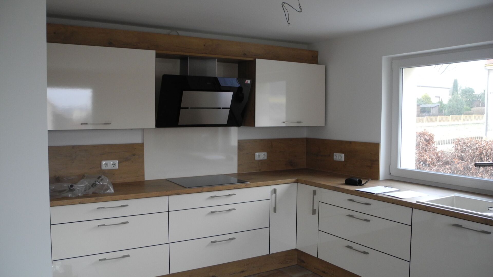 Moderne Küche mit weißen Schränken, Holzelementen und einer Dunstabzugshaube.