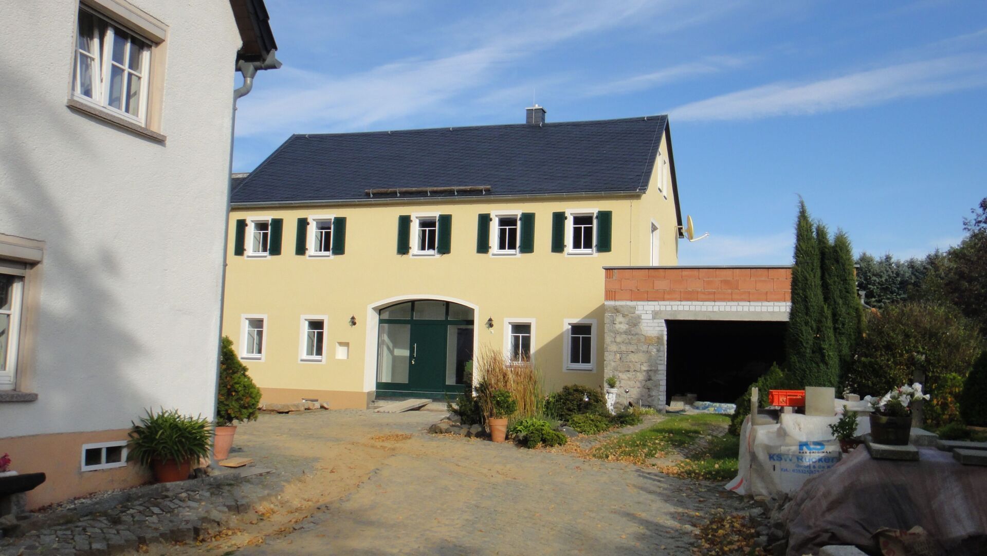 Gelbes Haus mit grünen Fensterläden, Garage und Kiesauffahrt an einem sonnigen Tag.