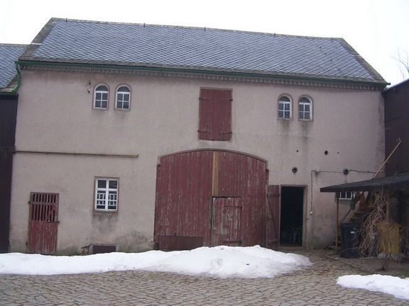 Eine rote Scheune mit einer großen zentralen Tür, kleinen Fenstern und Schnee auf dem Boden.