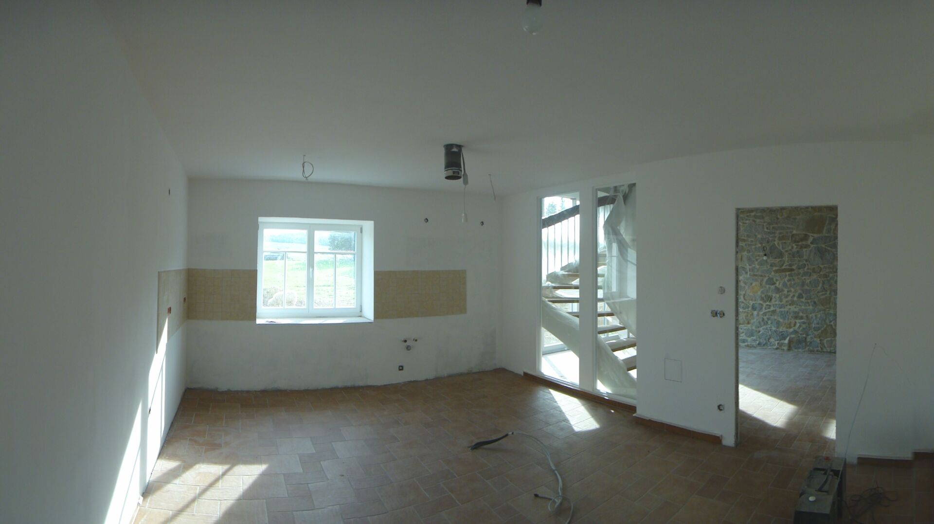 Leerer Raum mit Fenster, Treppe und offener Tür; unfertige Wände, Sonnenlicht.