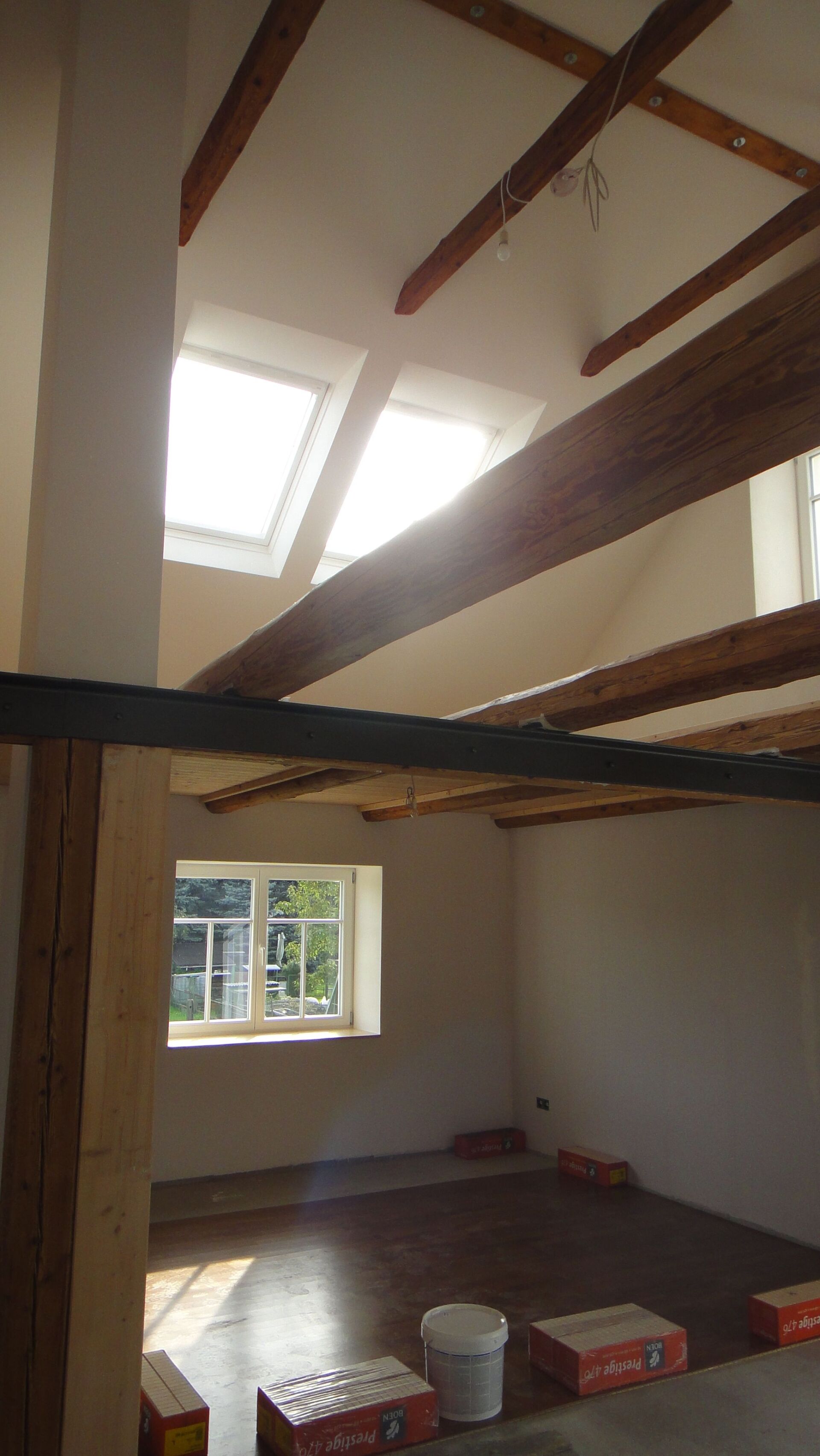 Innenansicht eines im Bau befindlichen Raumes mit freiliegenden Holzbalken, natürlichem Licht durch Oberlichter und Fenster.