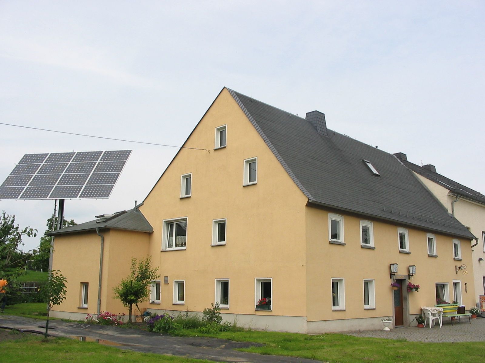 Gelbes Gebäude mit dunklem Dach, daran befestigtes Solarpanel.