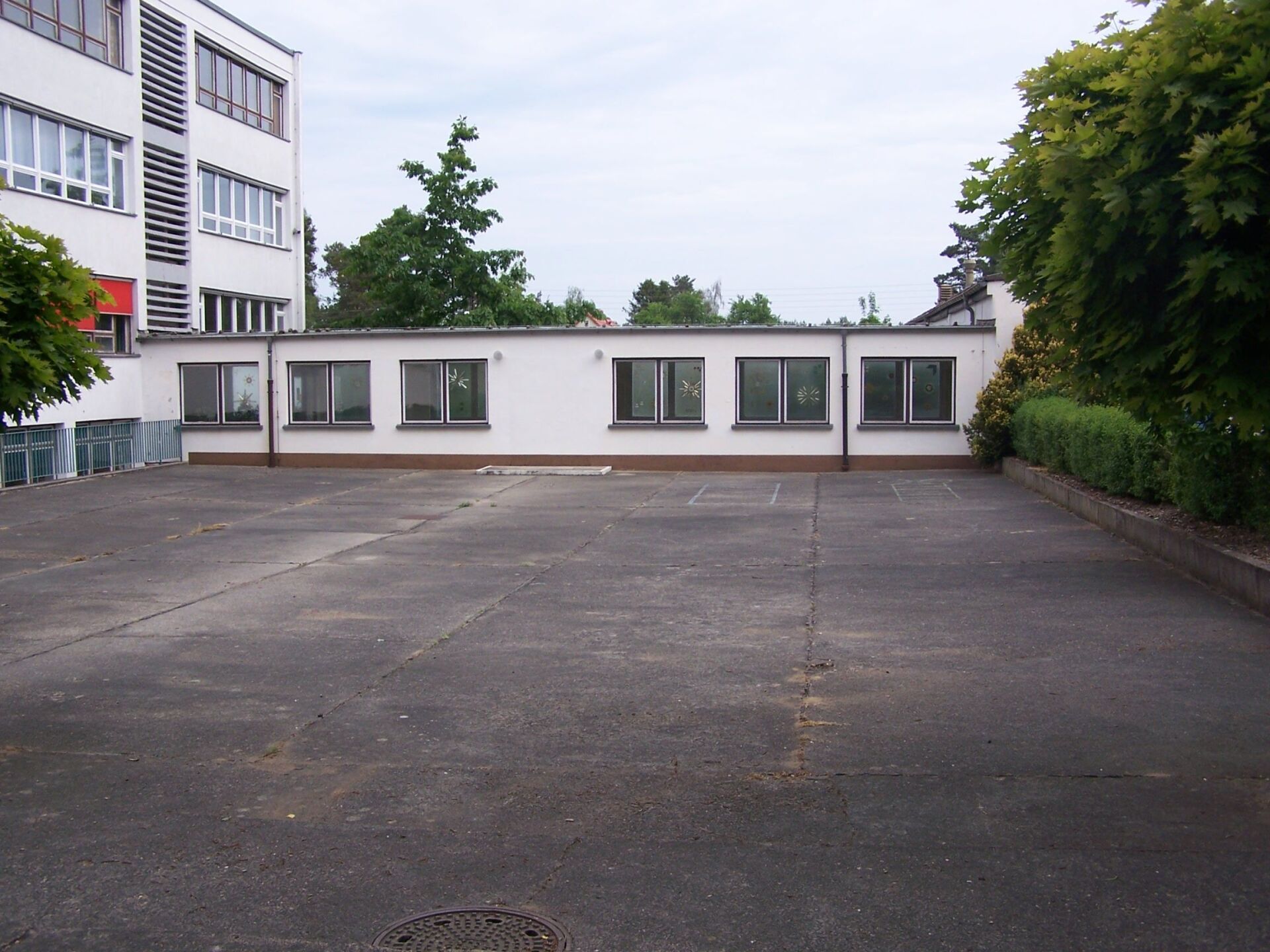 Ein leeres Betongrundstück mit einem niedrigen weißen Gebäude und jeweils einem mehrstöckigen Gebäude an den Seiten.