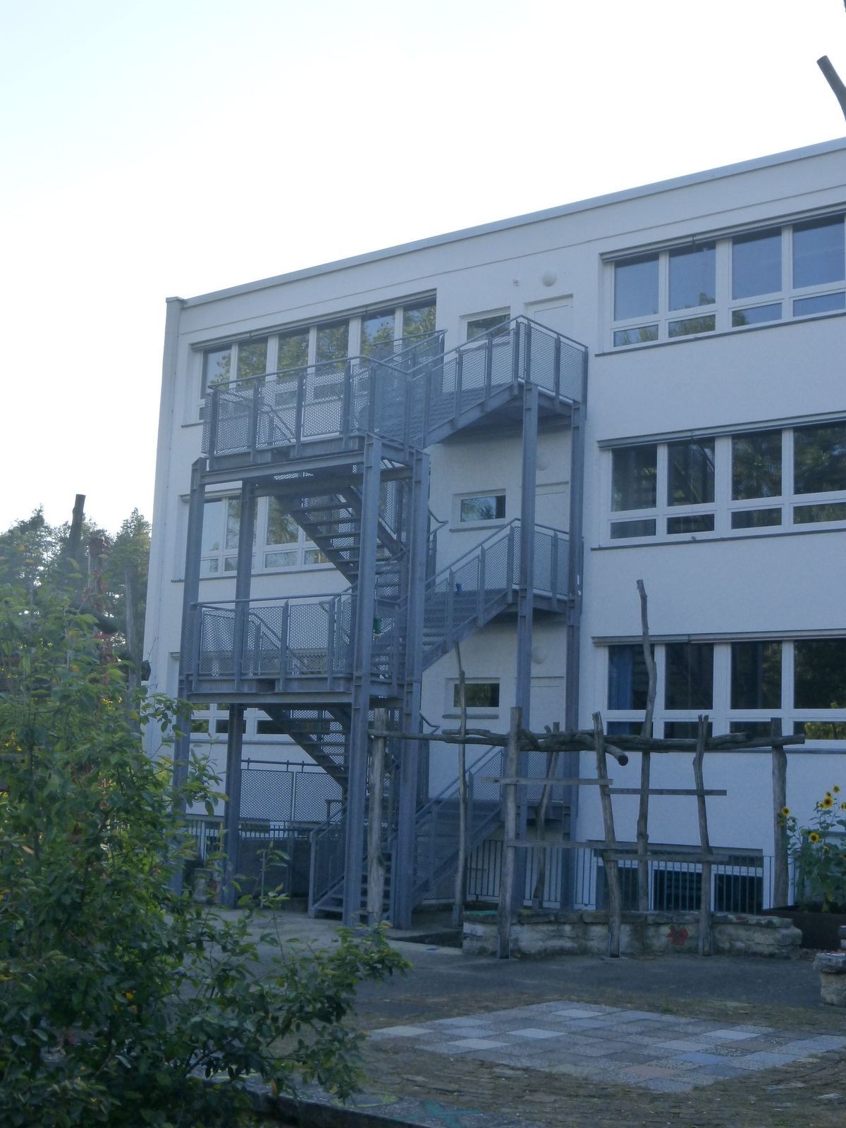 Eine metallene Feuertreppe an der Seite eines weißen Gebäudes mit vielen Fenstern, die an einem bewölkten Tag gut zu sehen ist.