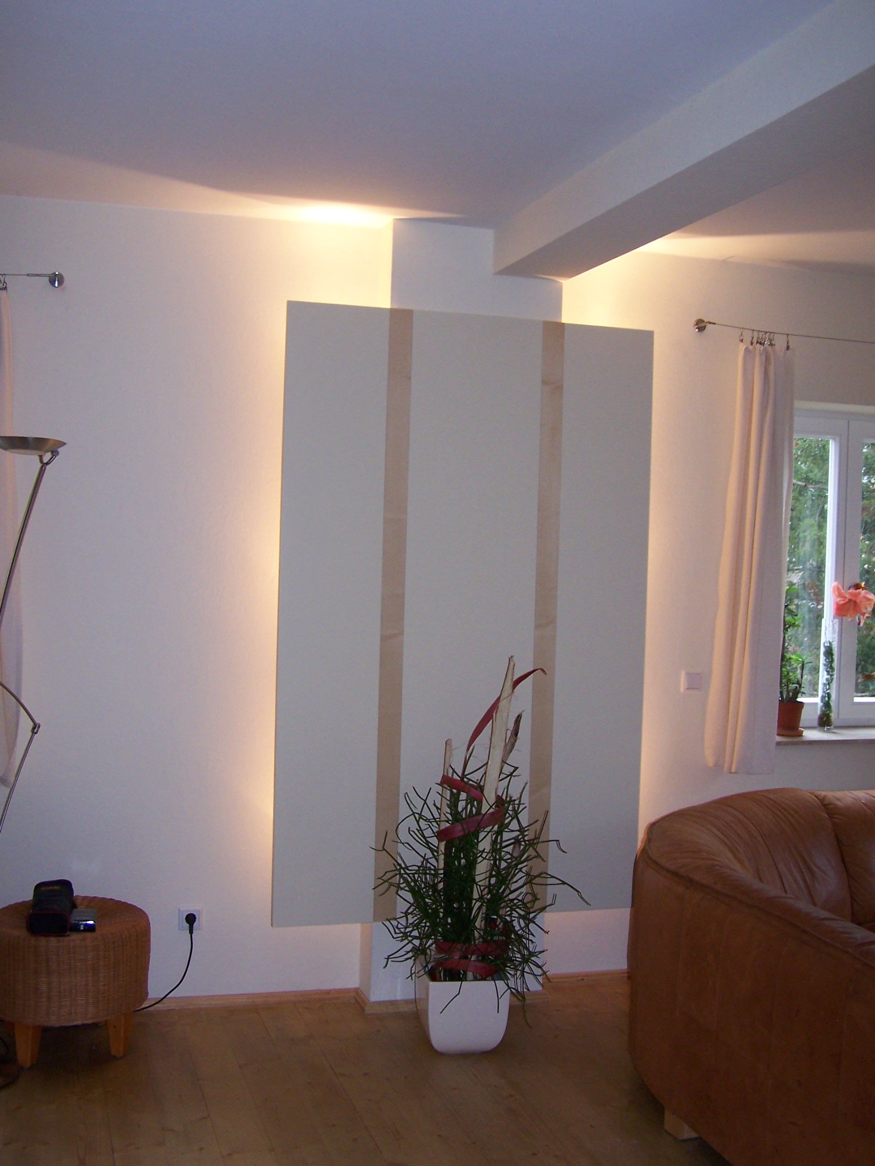 Interieur mit cremefarbener Wand, Wandpaneel mit vertikalen hellbraunen Streifen, Blumenarrangement, Ledersofa und Korbhocker.