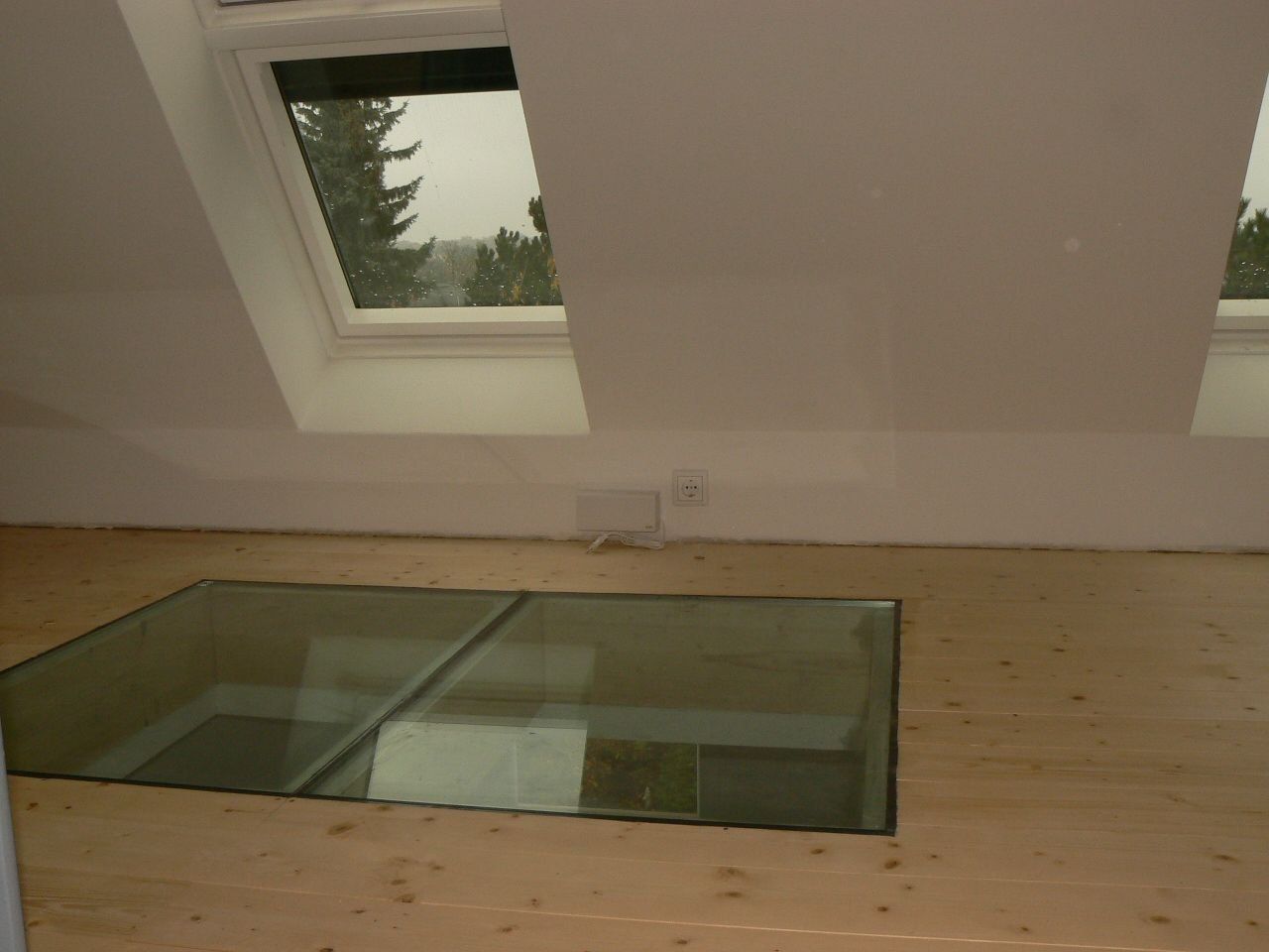 Innenansicht eines Dachgeschosses mit Oberlicht und Glasboden. Naturholzboden und weiße Wände.