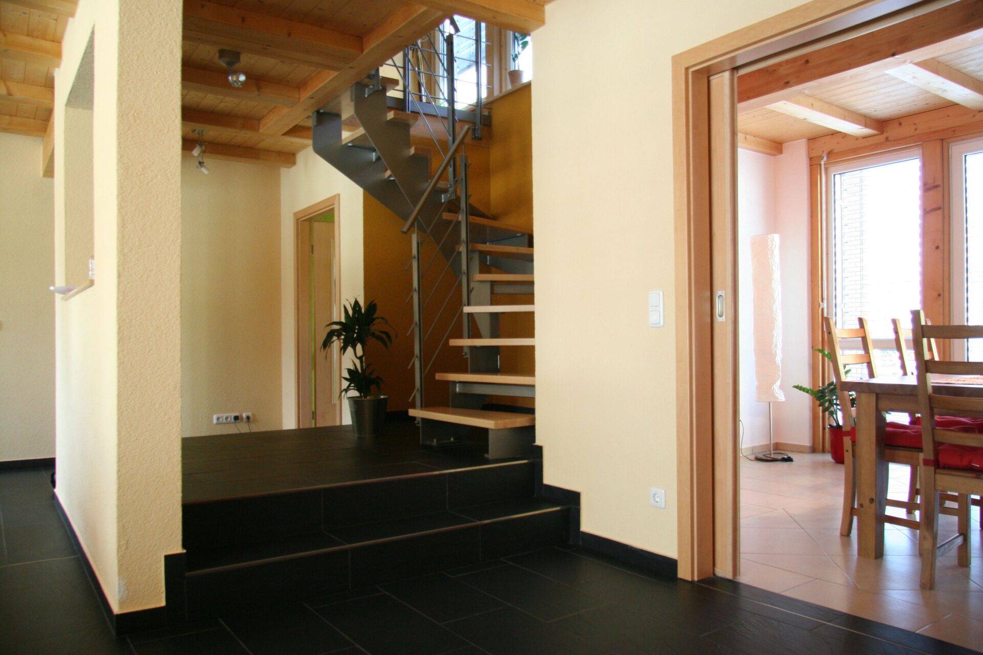 Interieur mit schwarzem Fliesenboden, Treppe und Holzdecke in einem modernen Haus.
