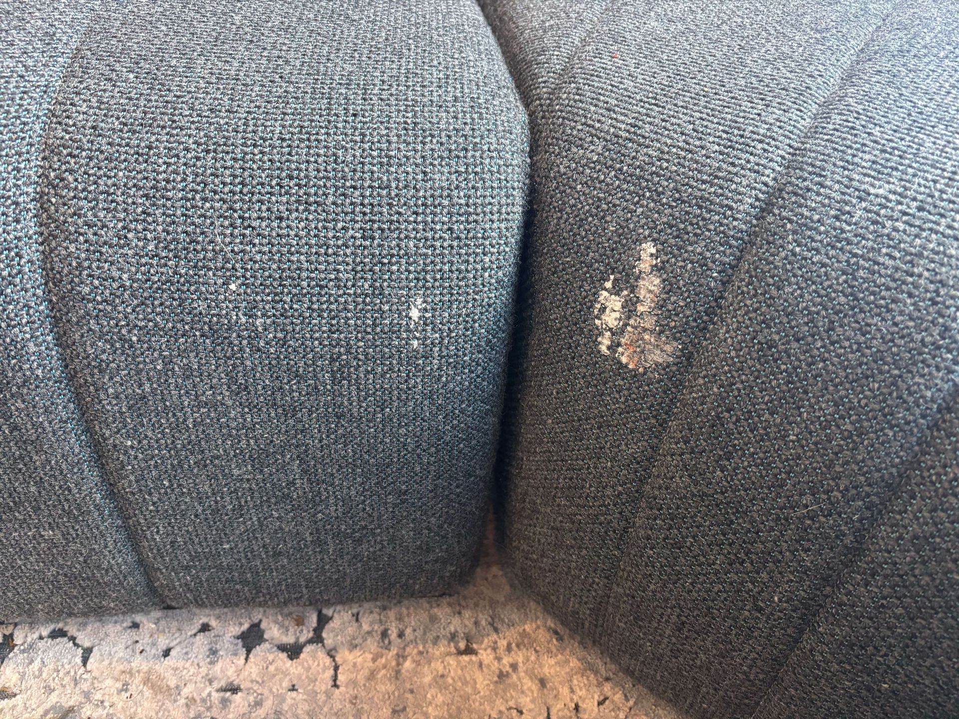 Close-up of a blue-gray fabric sofa with white spots on the armrest. The sofa is in an interior setting.