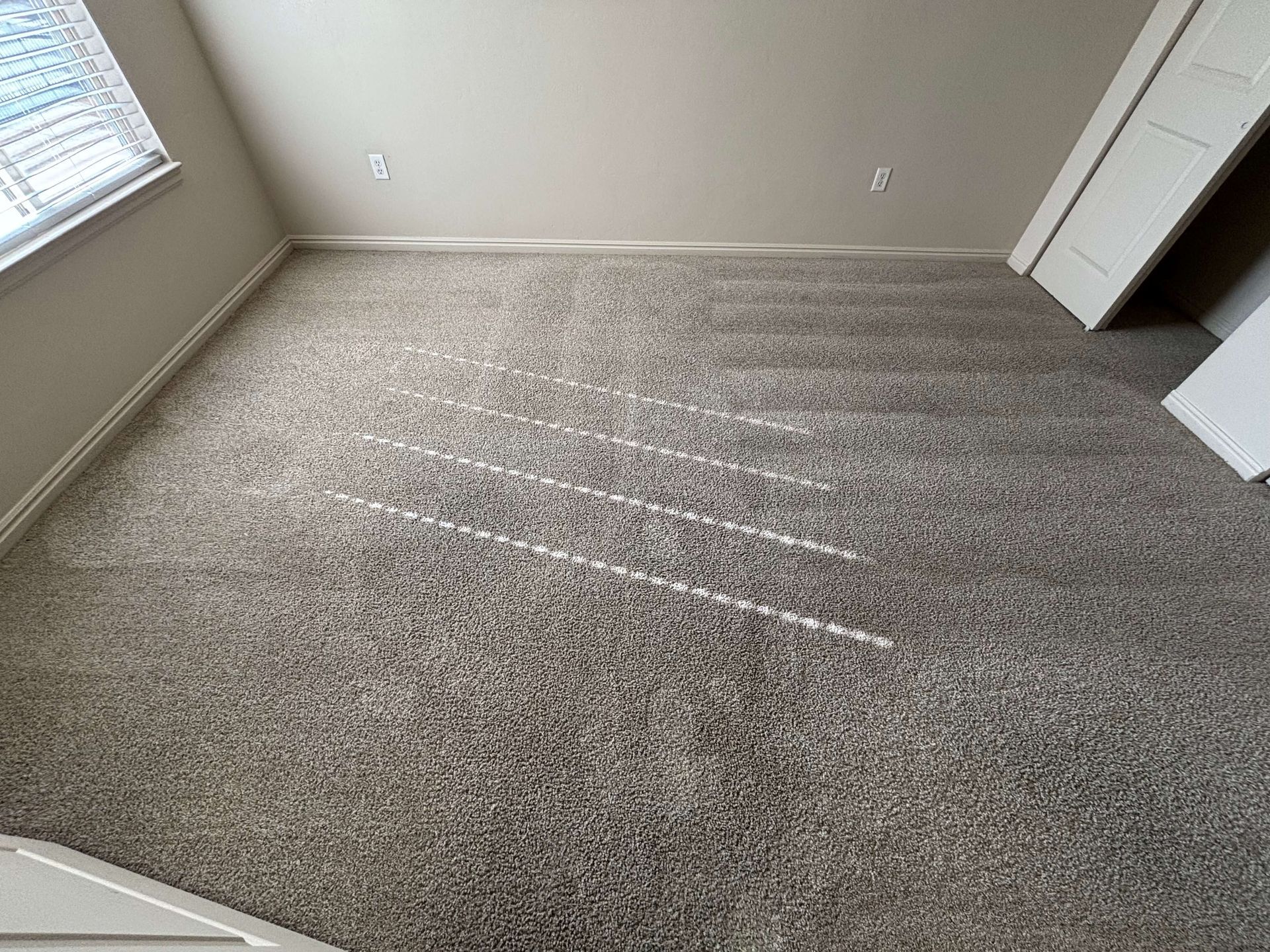 A room with beige walls and gray carpet, lit by sunlight through a window. White doors lean against a wall.