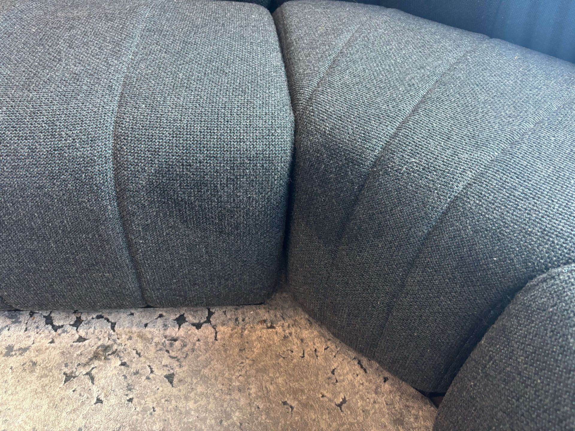 Close-up of a dark gray fabric sofa with textured surface. The sofa sections are joined. Beige floor in foreground.