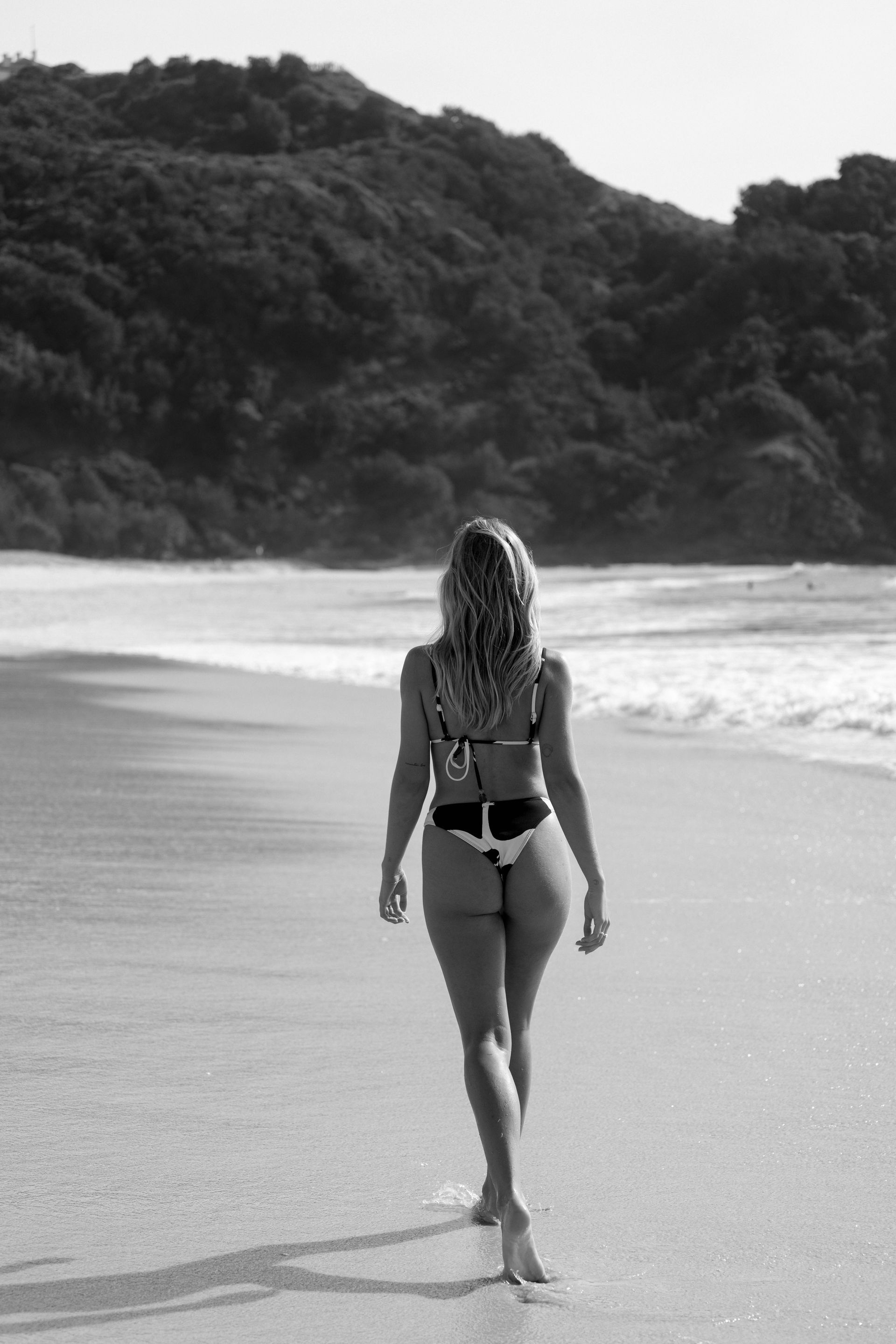 A woman in a bikini is walking on the beach.