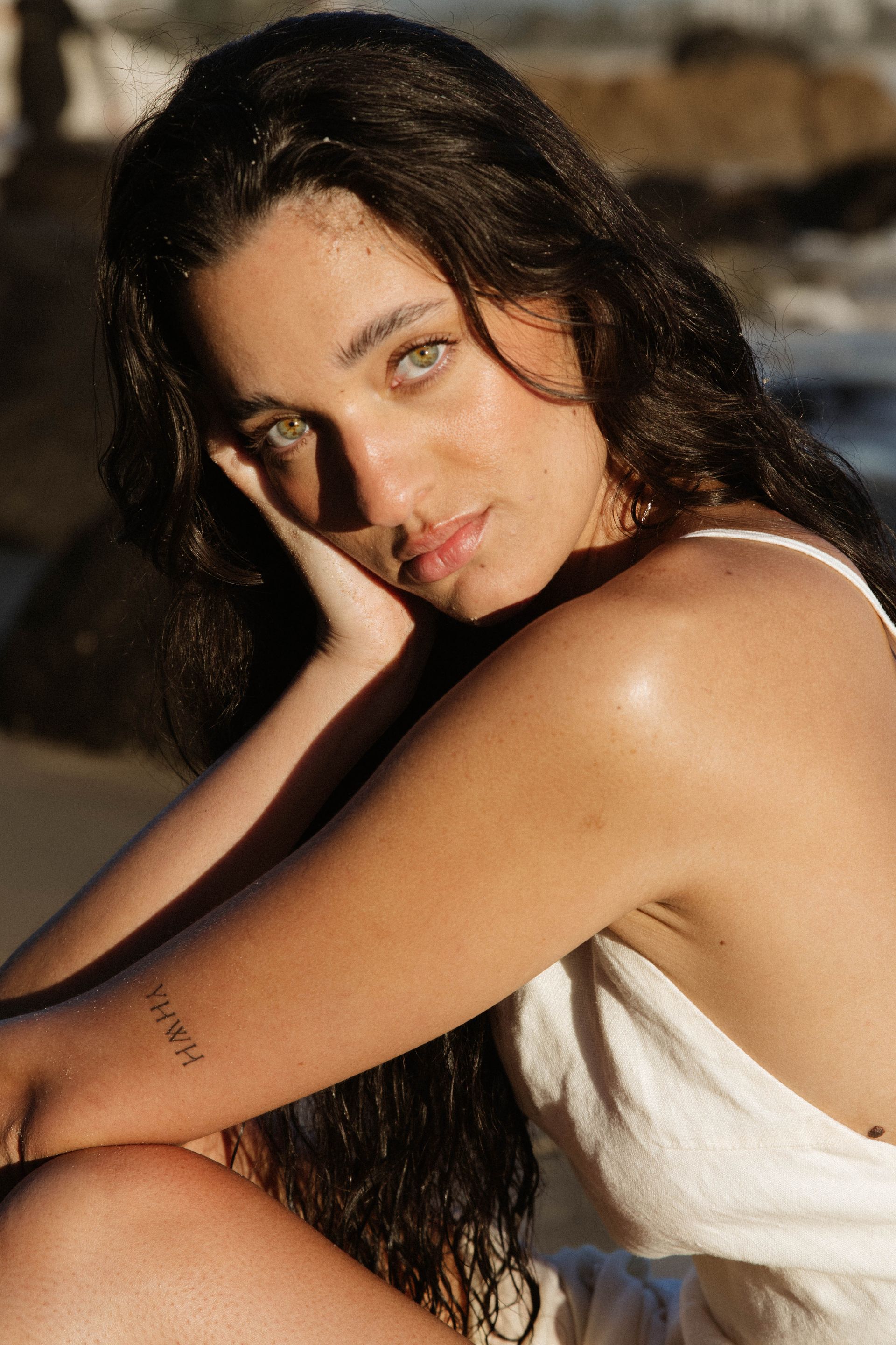 A woman with a tattoo on her arm is sitting on the beach.