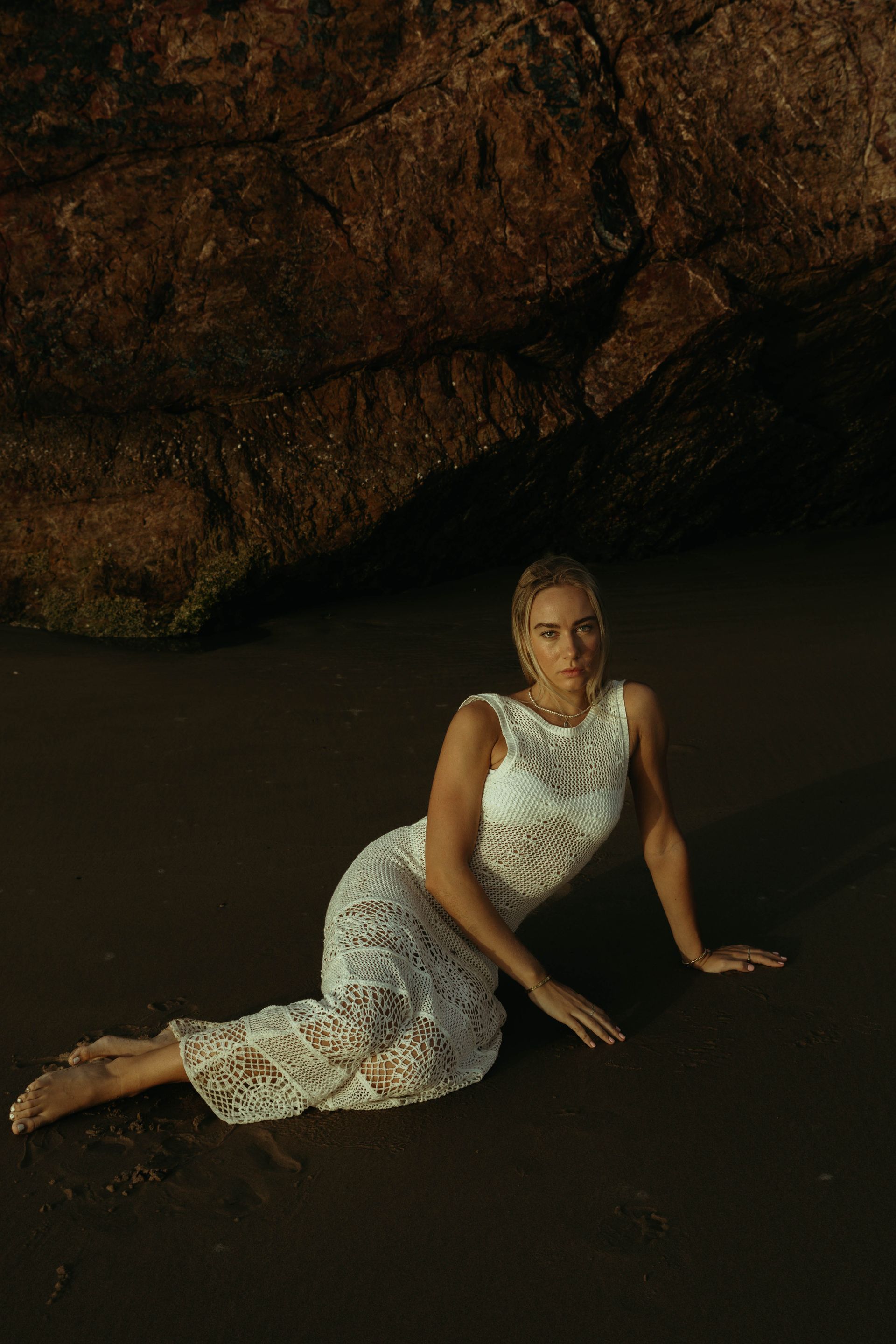 A woman in a white dress is kneeling on the beach.