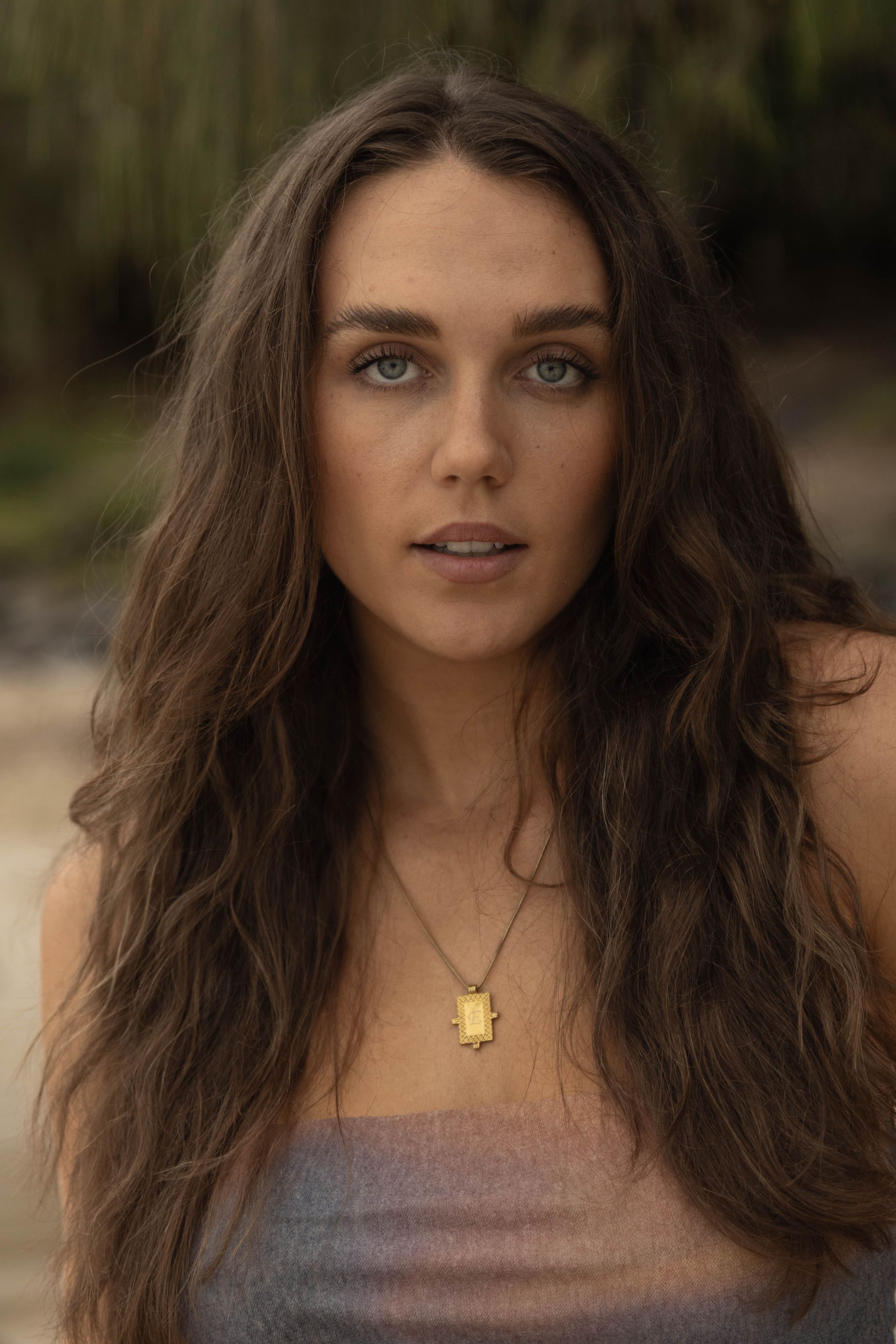 A woman with long hair is wearing a necklace and looking at the camera.