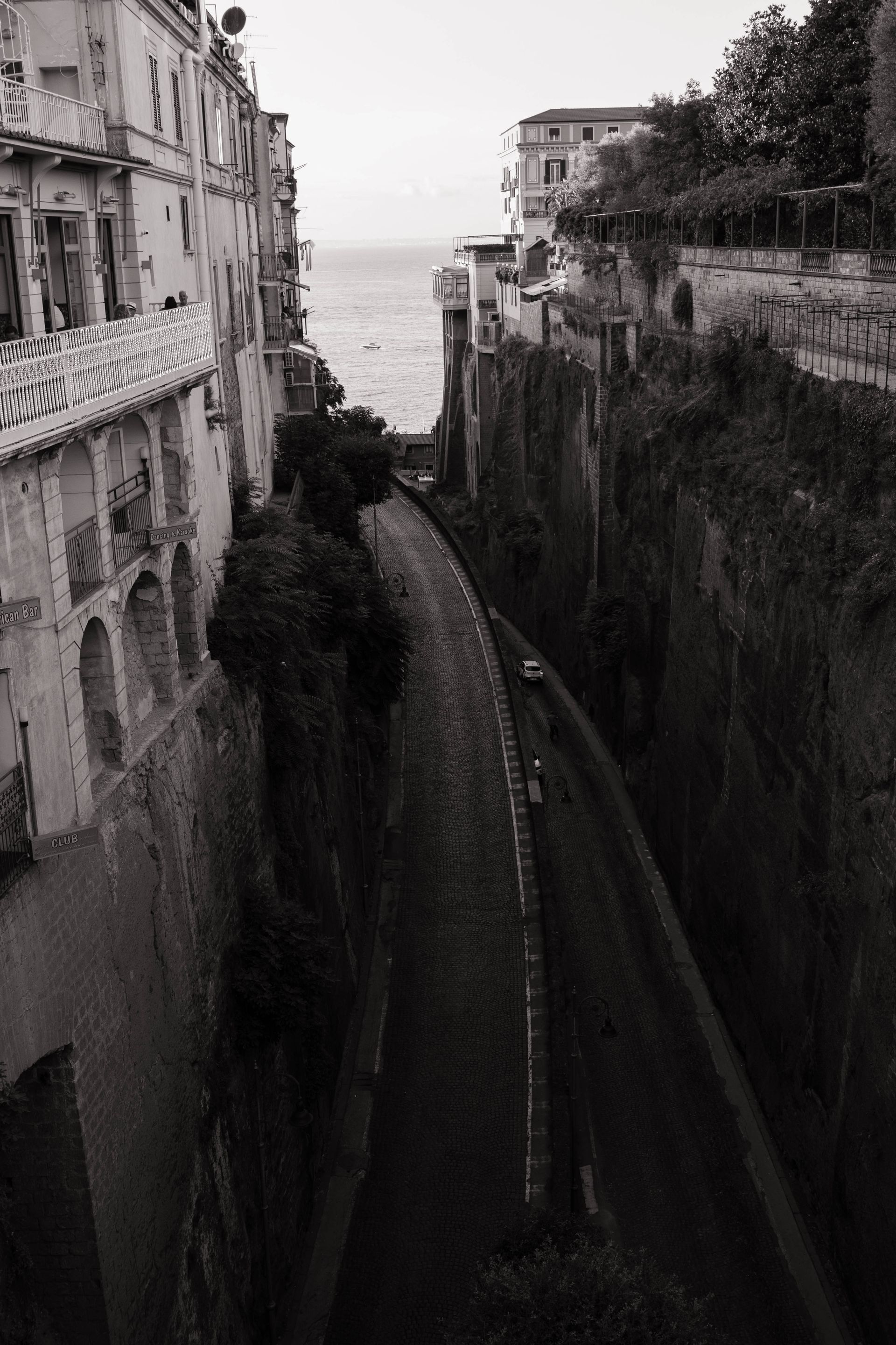 A black and white photo of a narrow alleyway leading to the ocean