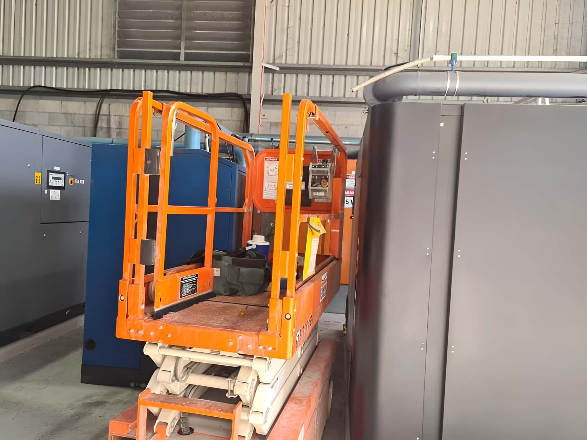 A Scissor Lift Is Parked In A Warehouse Next To A Machine — Gladstone Sheet Metal Pty Ltd In Gladstone Central, QLD