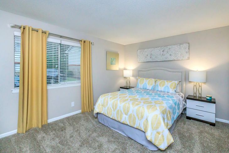 Bedroom with yellow curtains, bed with patterned comforter, bedside tables, and artwork.