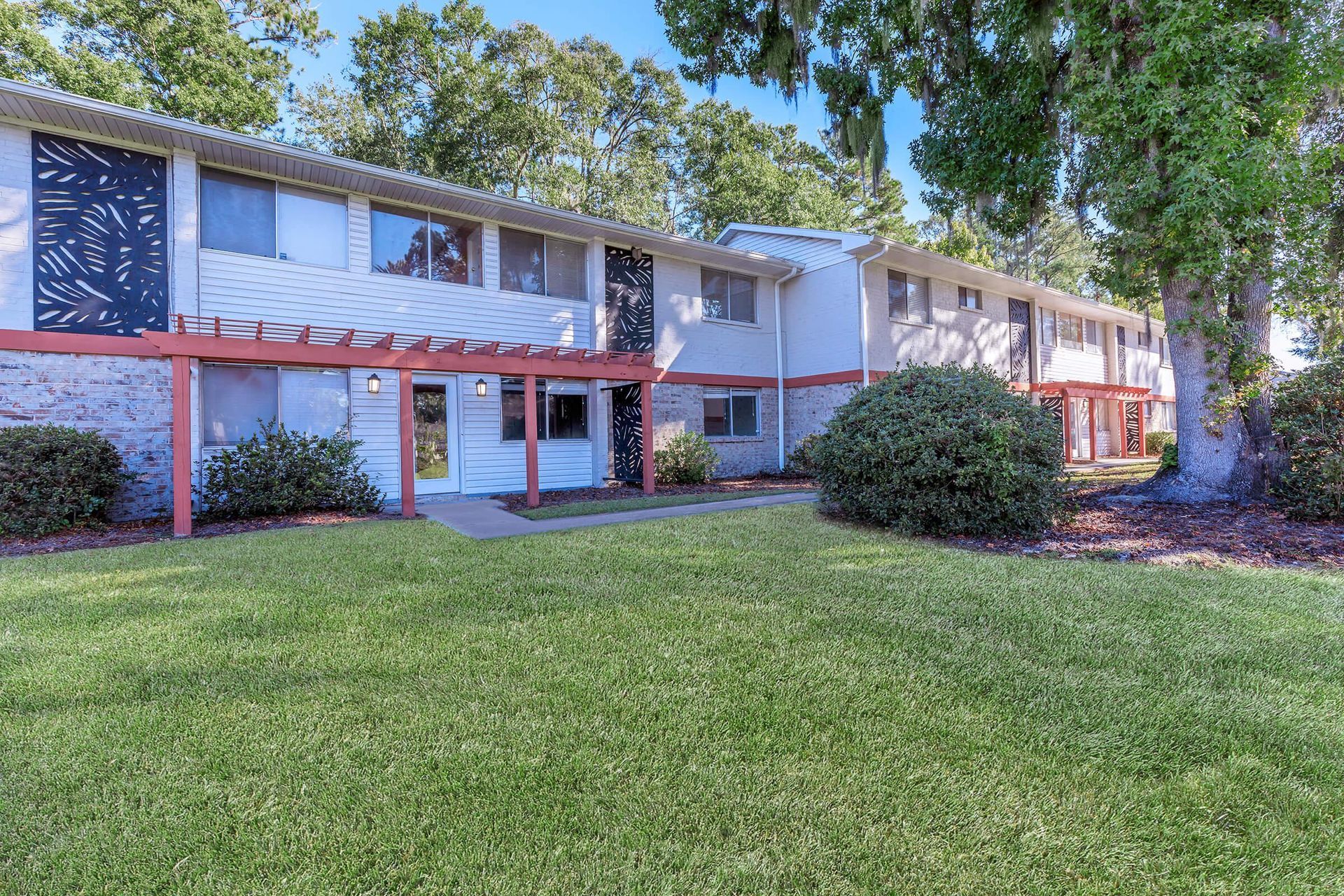 Two-story apartment building with white siding, red trim, and a grassy lawn.