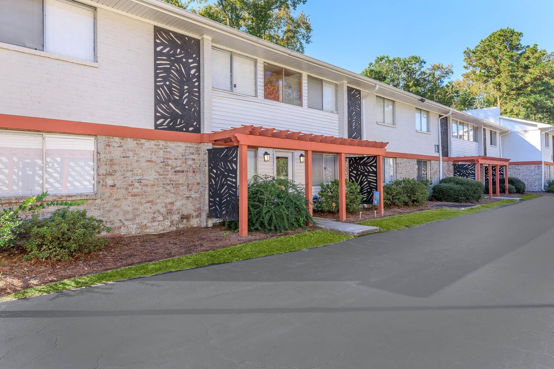 Row of white townhomes with orange trim, brick facade, and a concrete driveway.