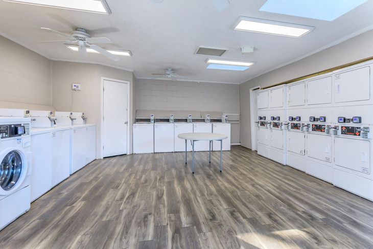 Laundry room with washers, dryers, and folding table. White cabinets and appliances. Gray wood flooring.