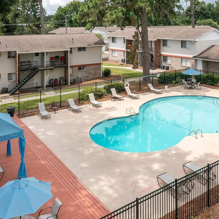 Apartment complex with a swimming pool. Lounge chairs surround the blue water. Sunny, outdoor setting.