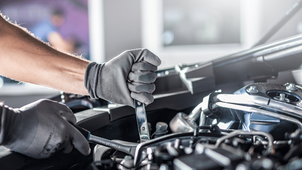 Mechanic's gloved hands using a wrench on a car engine in a well-lit garage.