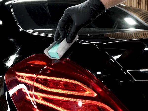 A gloved hand applies a detailing block to a car's taillight, showcasing a glossy black finish.