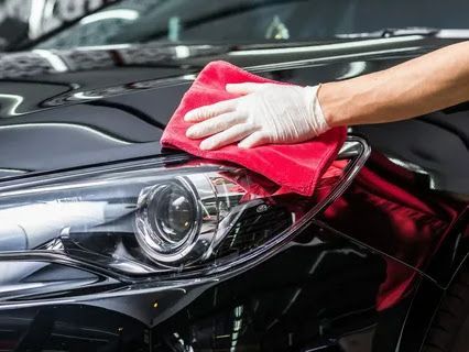 Gloved hand wiping a red cloth across the shiny hood of a black car, near a headlight.