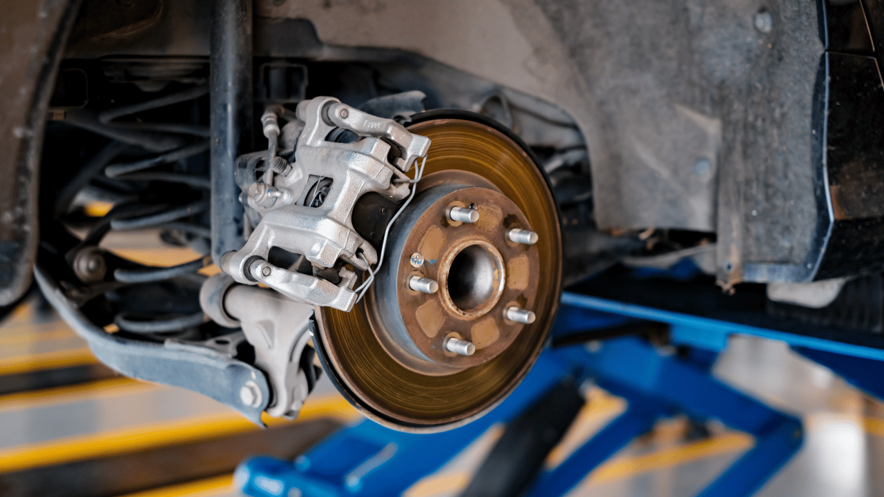 Car's rear brake assembly: rotor, caliper, spring, and hub, mounted on blue lift.