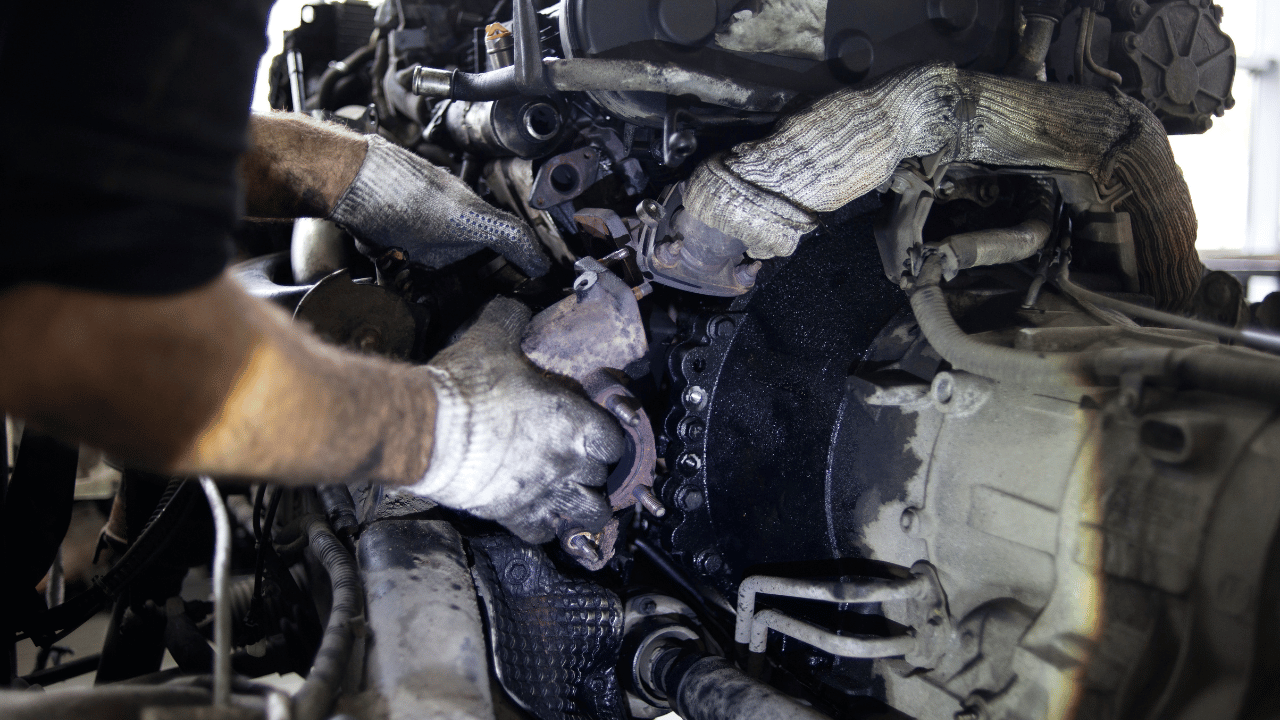 Mechanic working on a dirty car engine, wearing gloves.