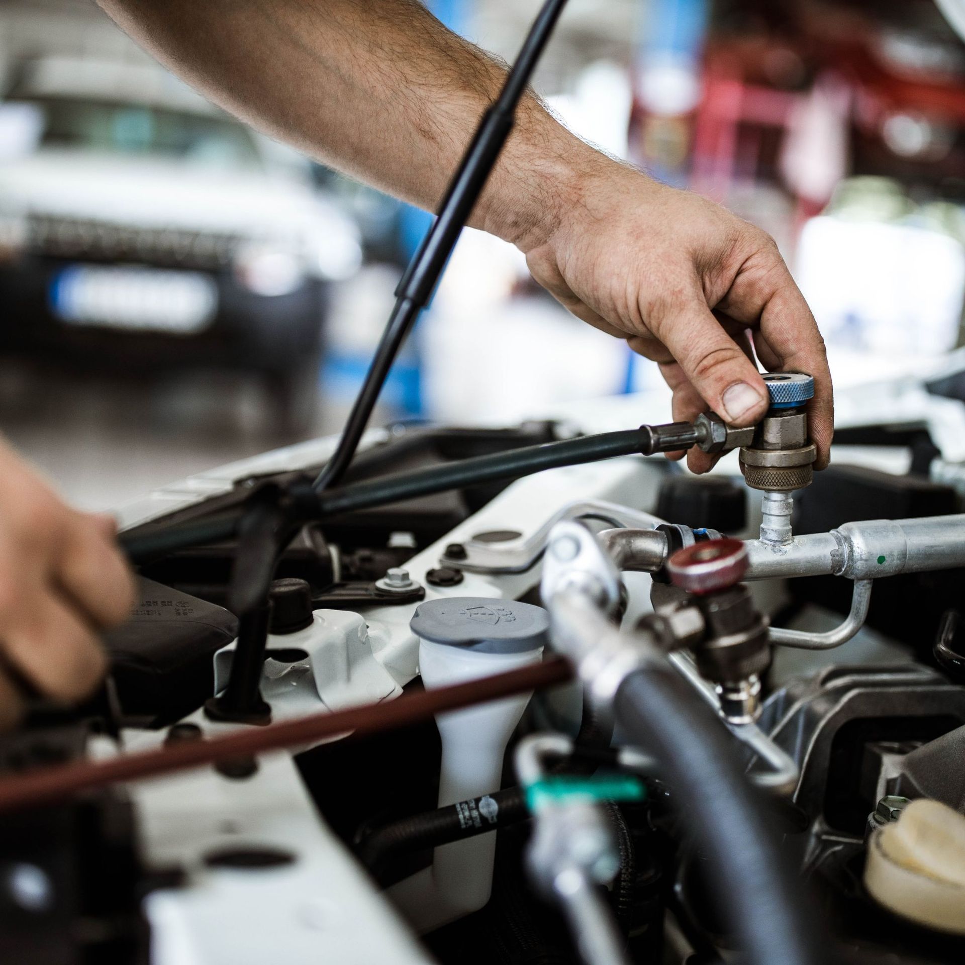 Mechanic working on a car engine, hands manipulating components in a garage setting.